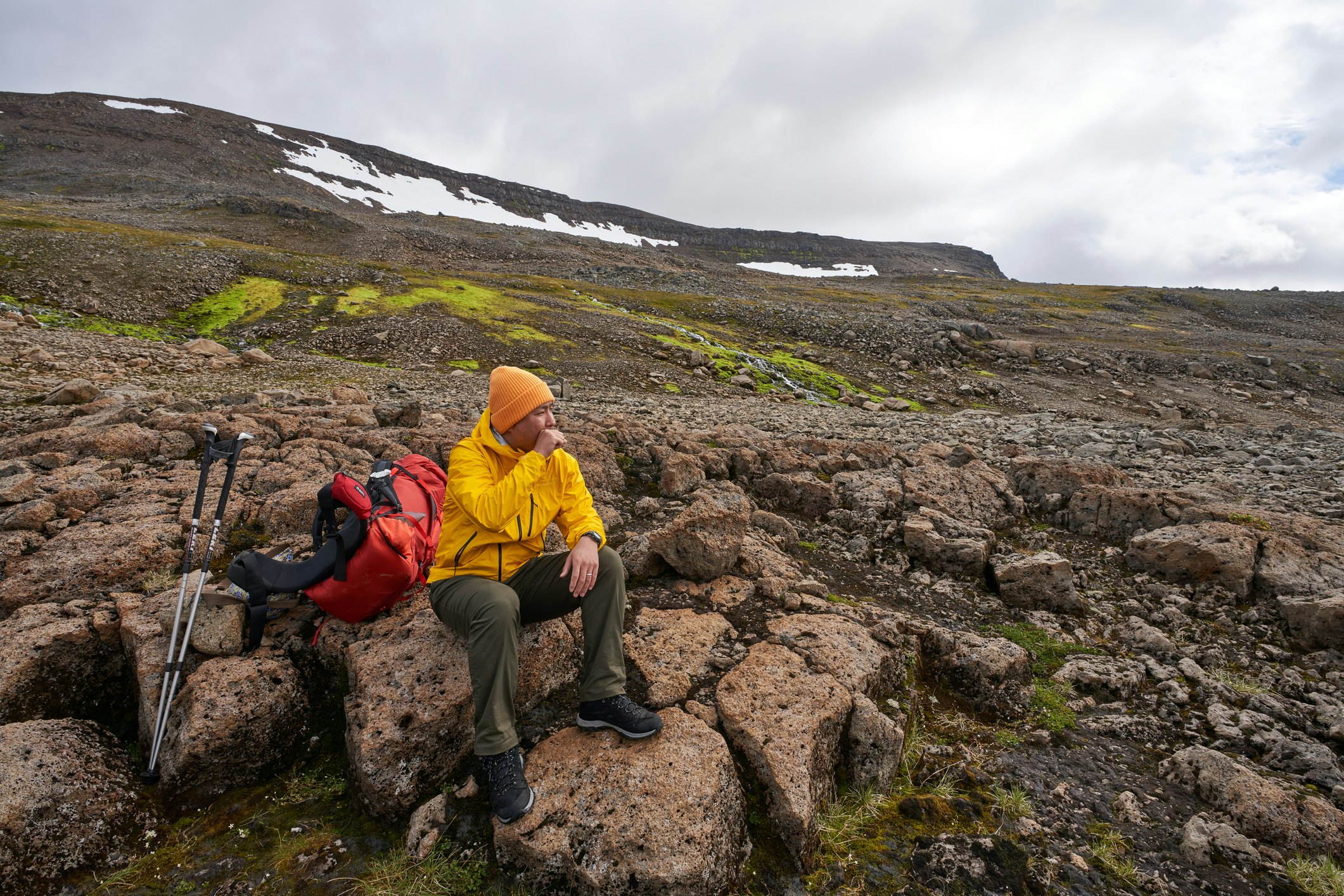 A man sits on a volcanic rock in Iceland, resting during a hike.