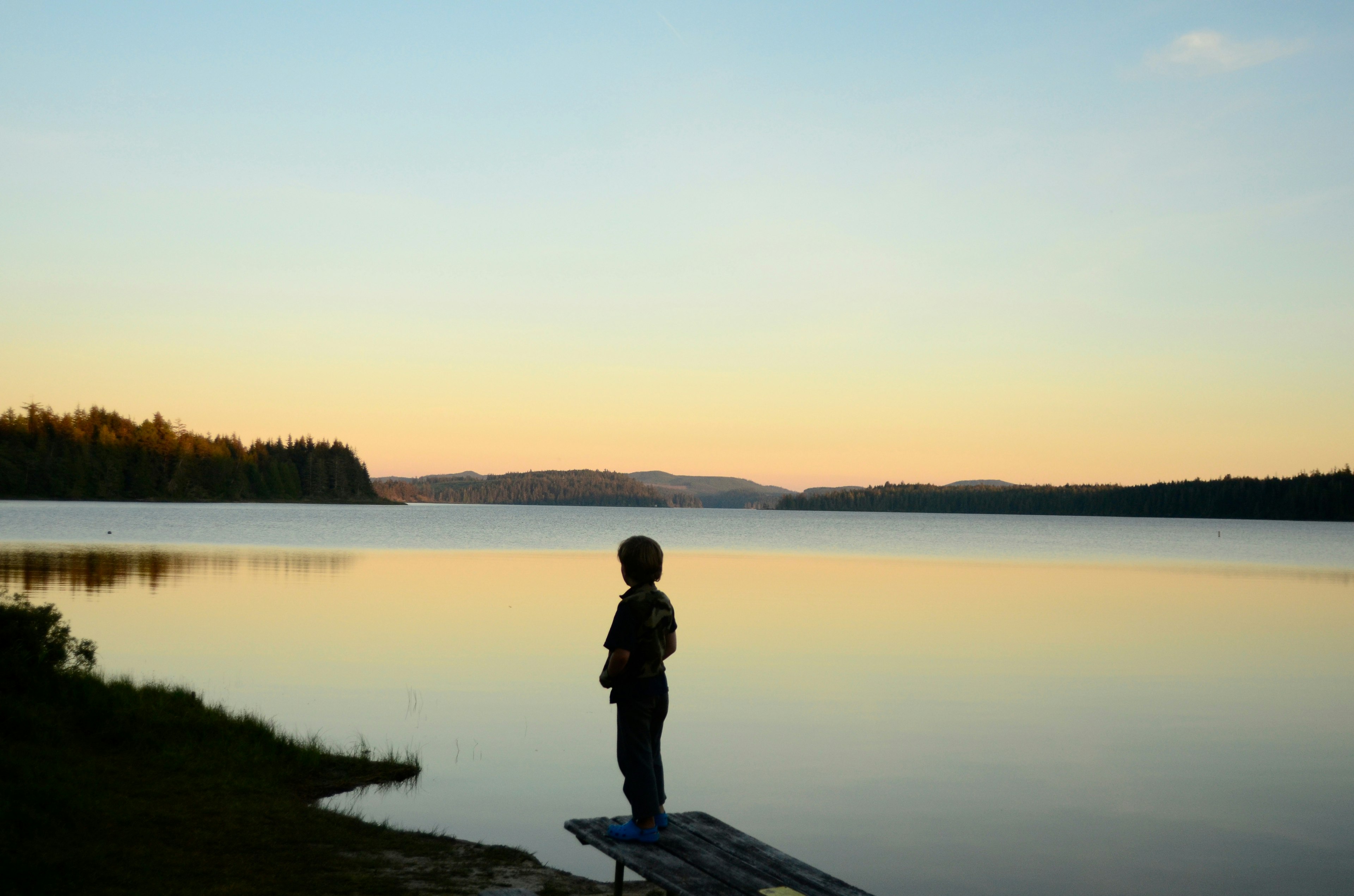 A figure in silhouette looks across a lake at sunset