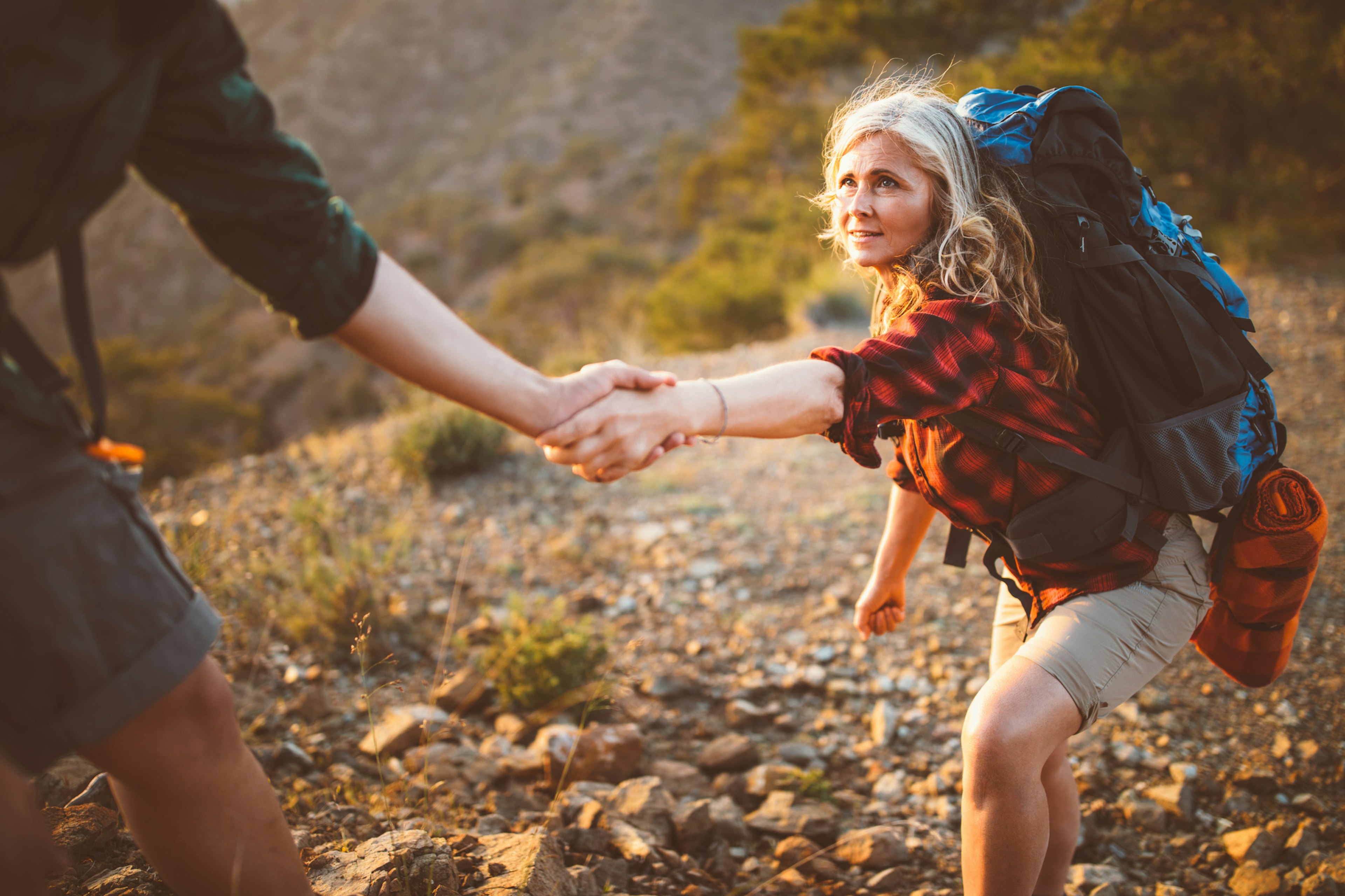 A woman hiker takes another hiker's hand when climbing up a steep section of rock in Cyprus