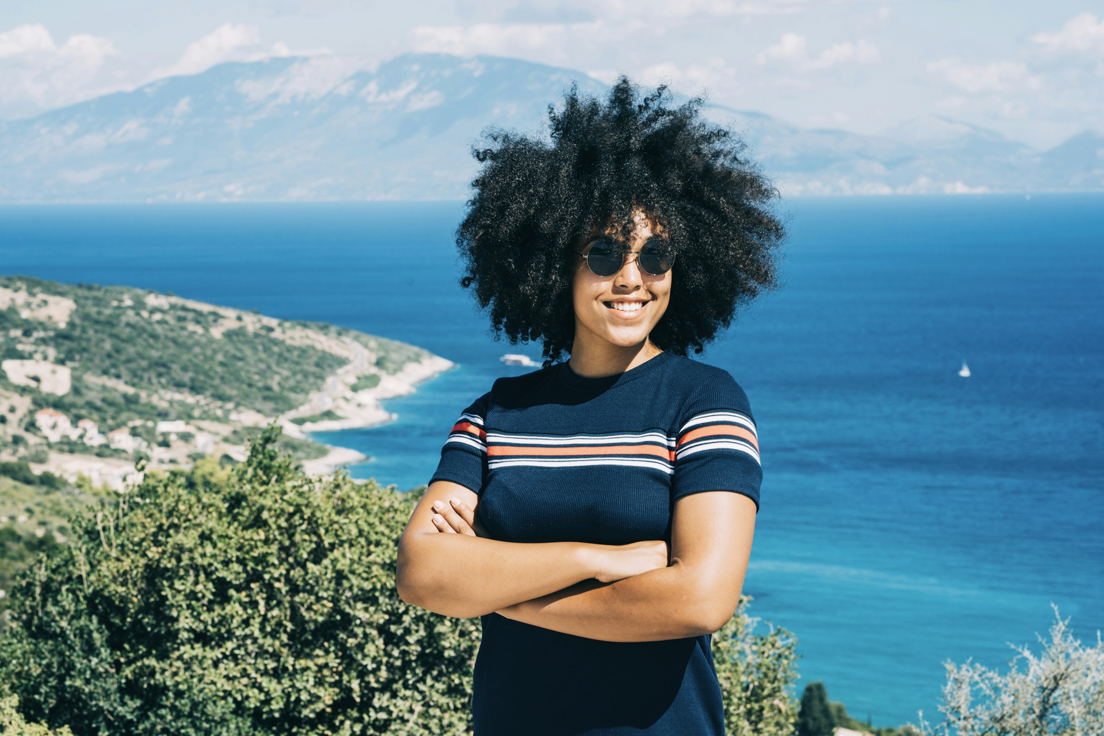 Smiling woman standing with her arms crossed with a view of the sea behind her