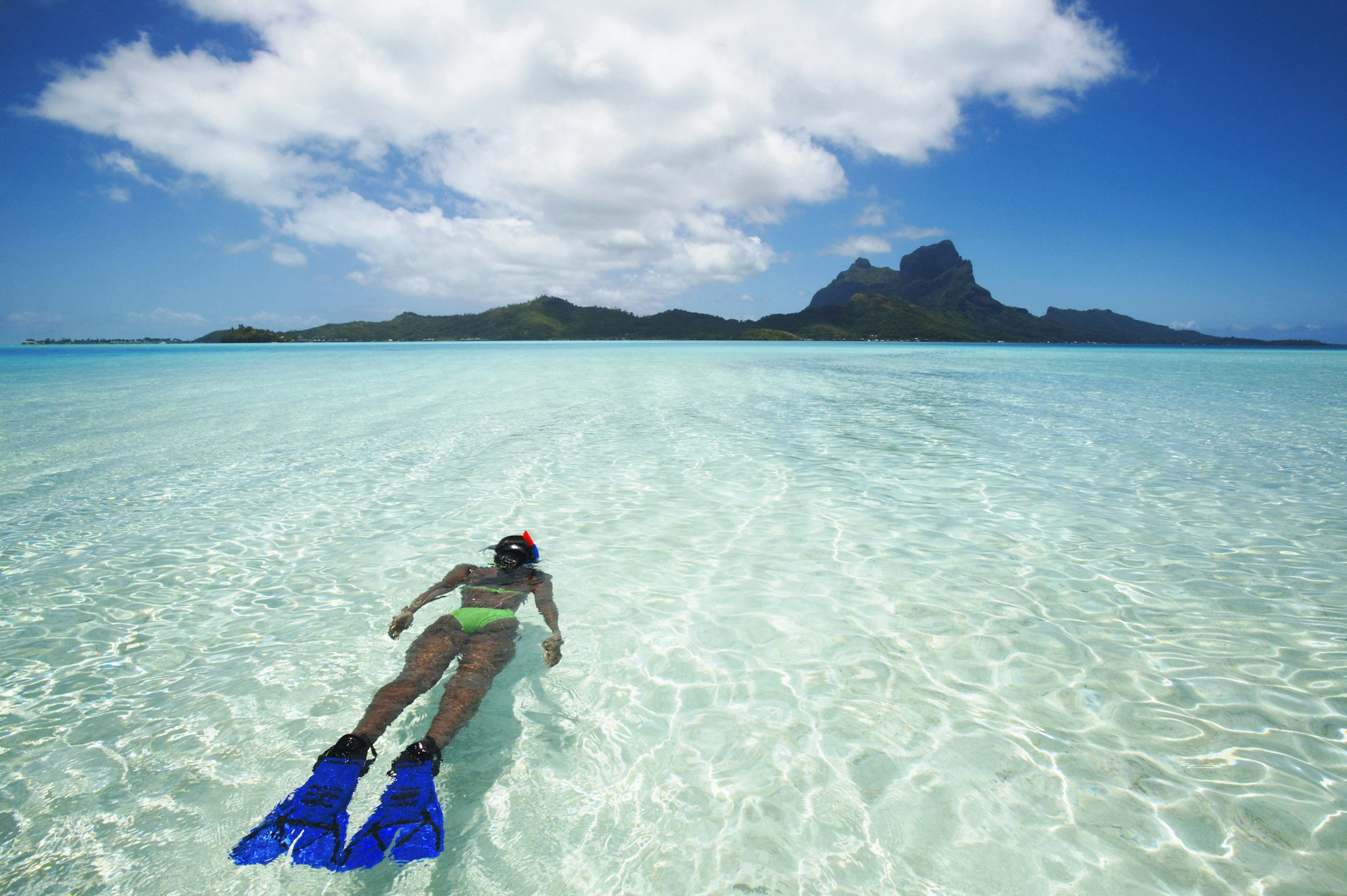 A woman snorkels in clear waters near an island with a jagged peak