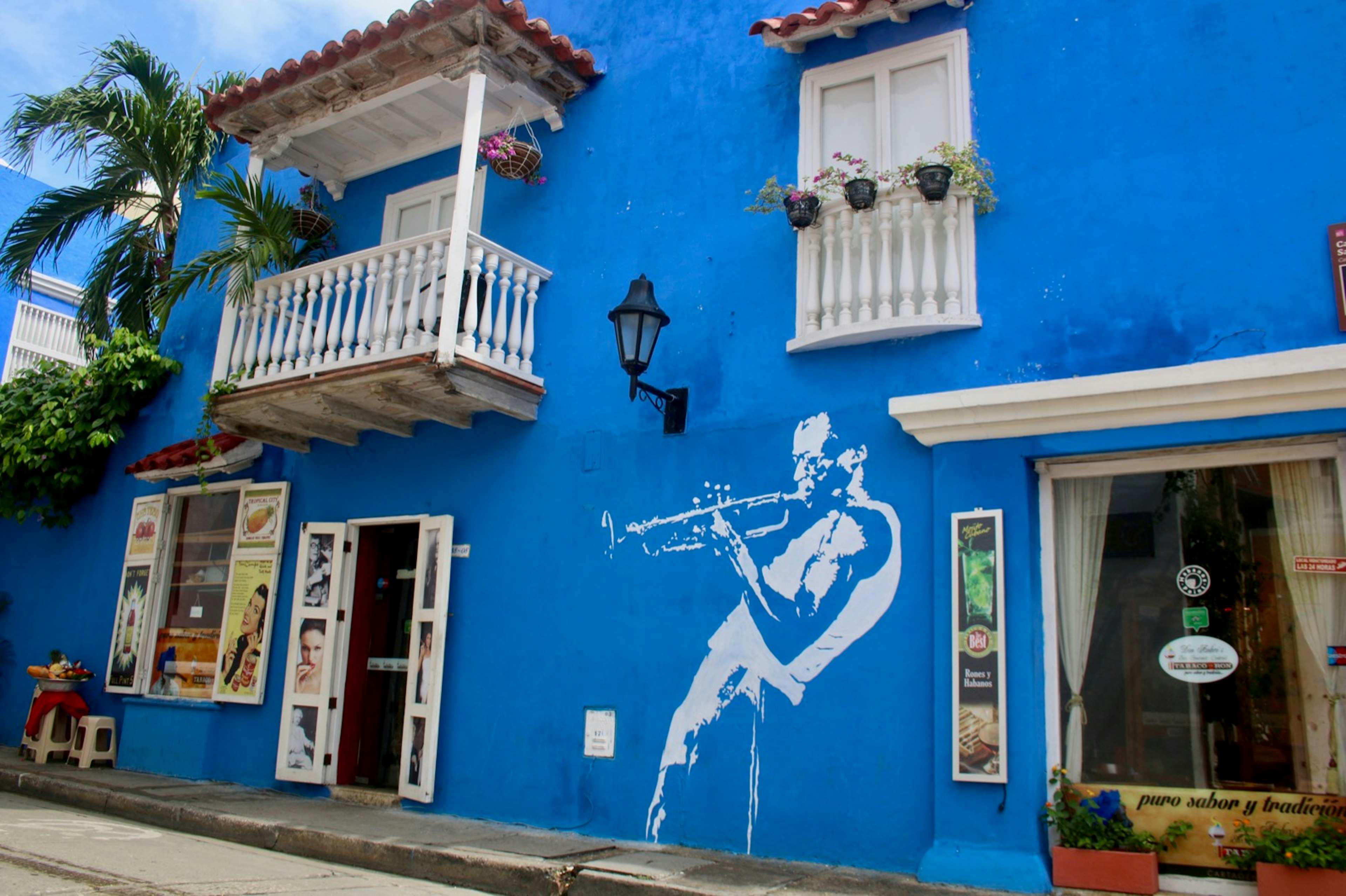 A blue wall containing a mural of a trumpet player, with a white balcony and window above; free things to do in Cartagena