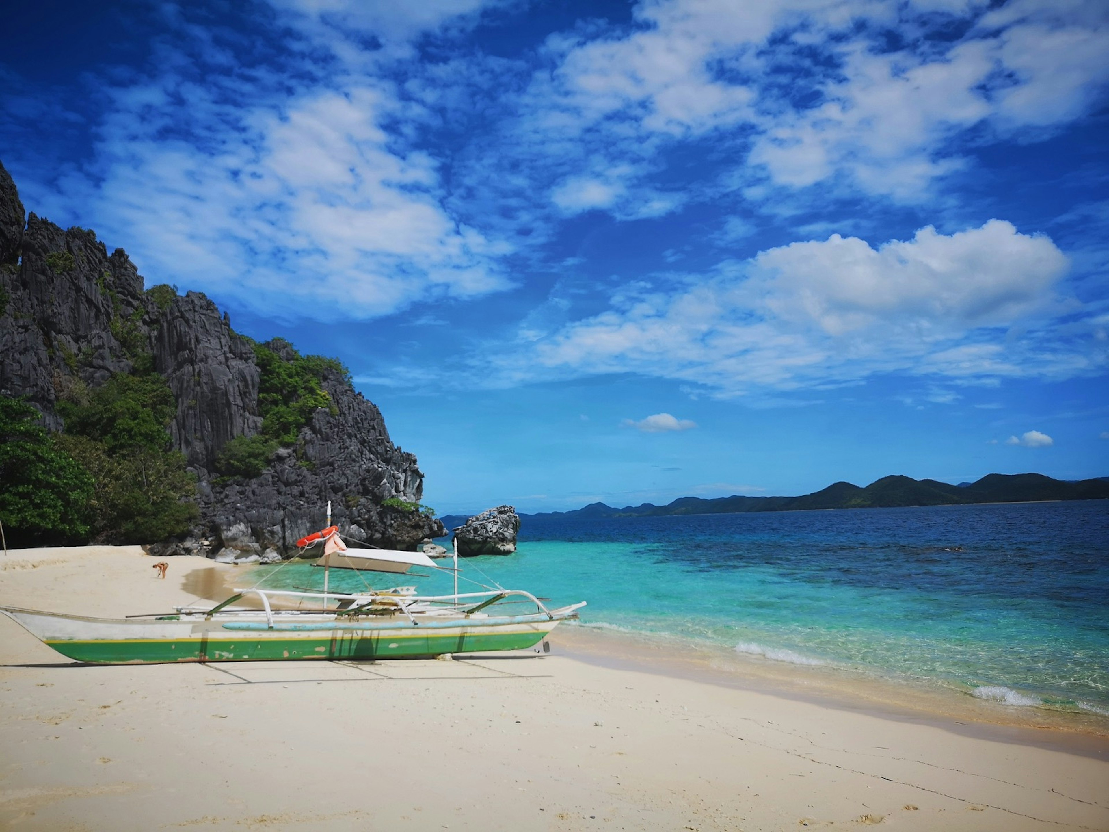 A catamaran rests on a white sand beach with a turquoise ocean and epic adventure beyond