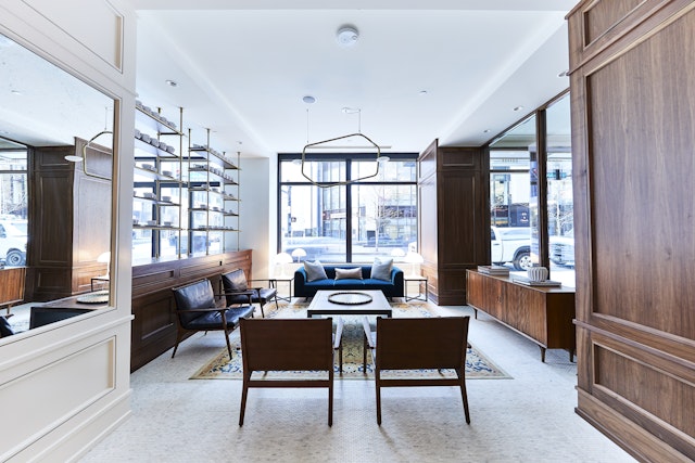 A blue velvet sofa sits at the far end of a white room full of mirrors and natural light with midcentury modern in a deep walnut tone