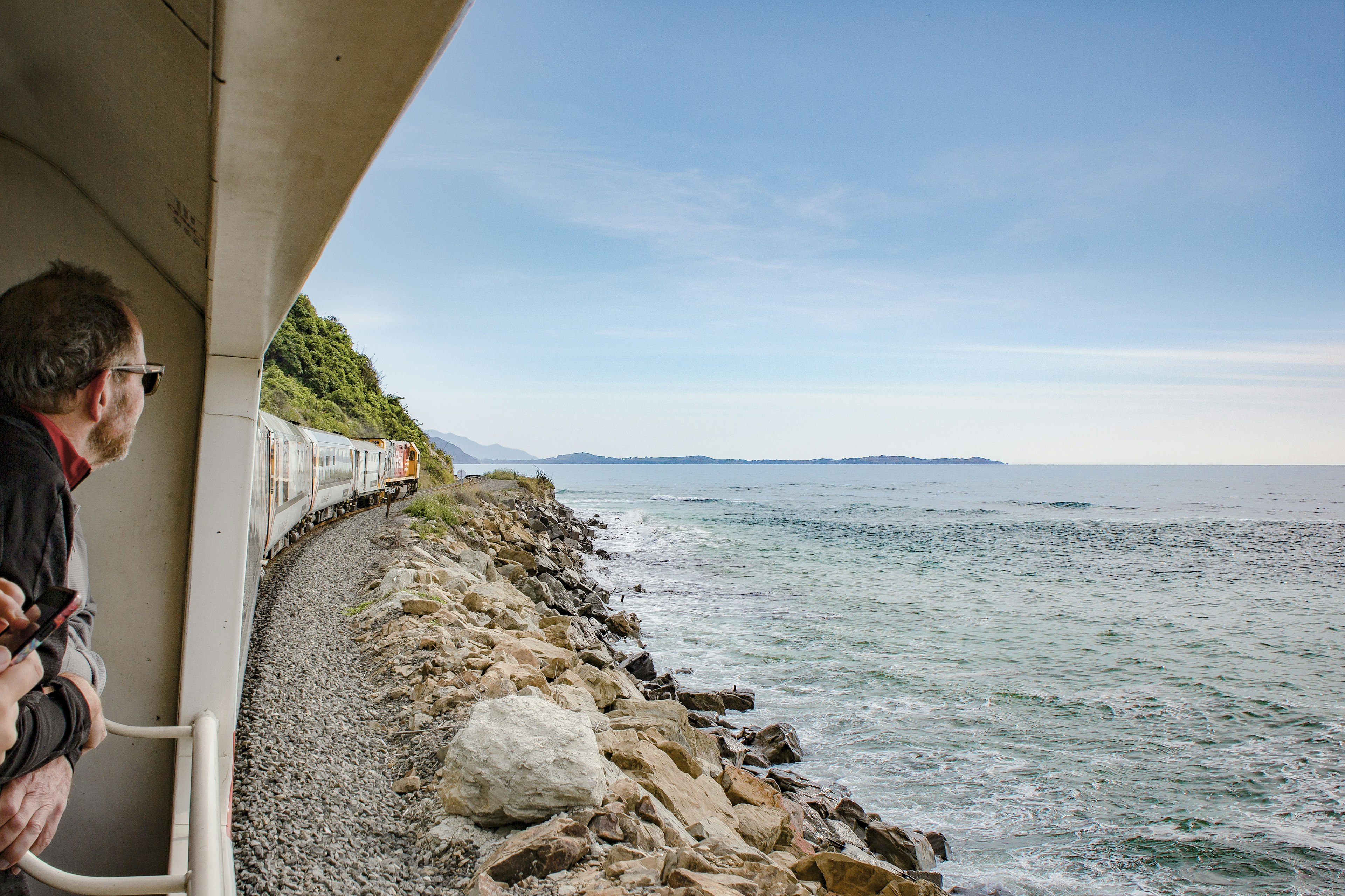 People look at coastal scenery from the open-sided carriage of a train