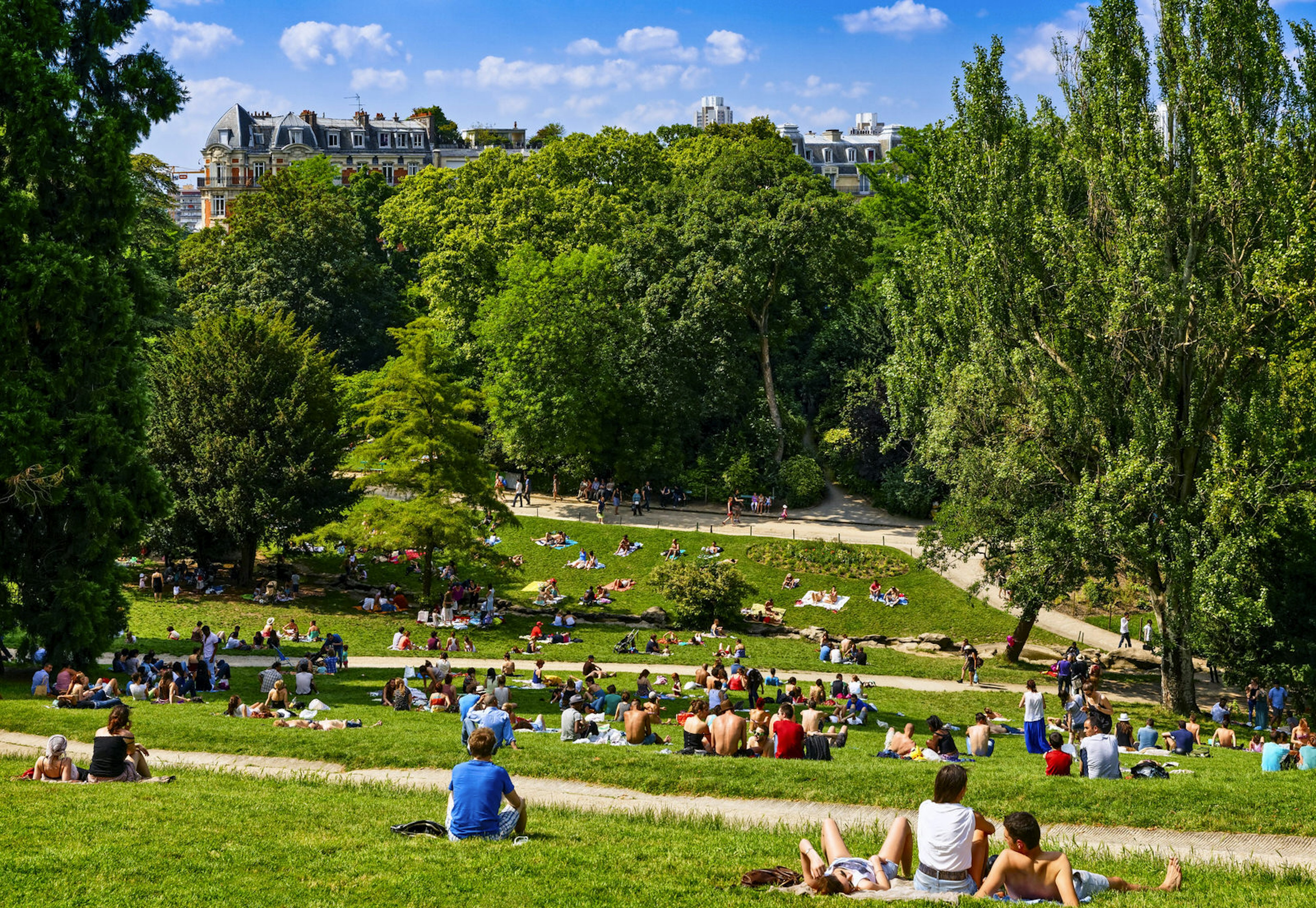 People lounge in the sun on the grass at Paris' Parc des Buttes Chaumont