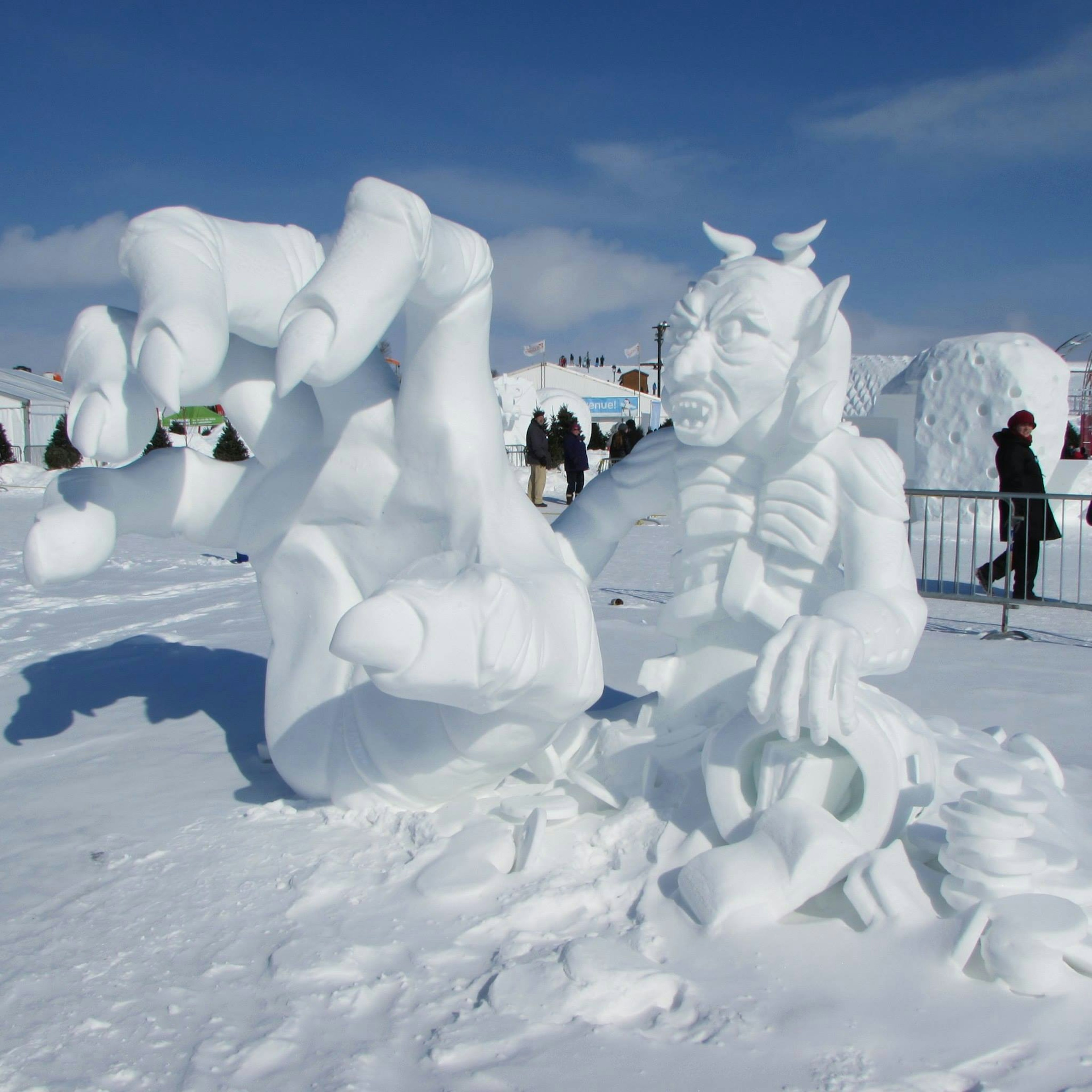 A larger-than-life size sculpture of a demon, with his hand outstretched to the camera, is carved from snow and ice in ϳé City.