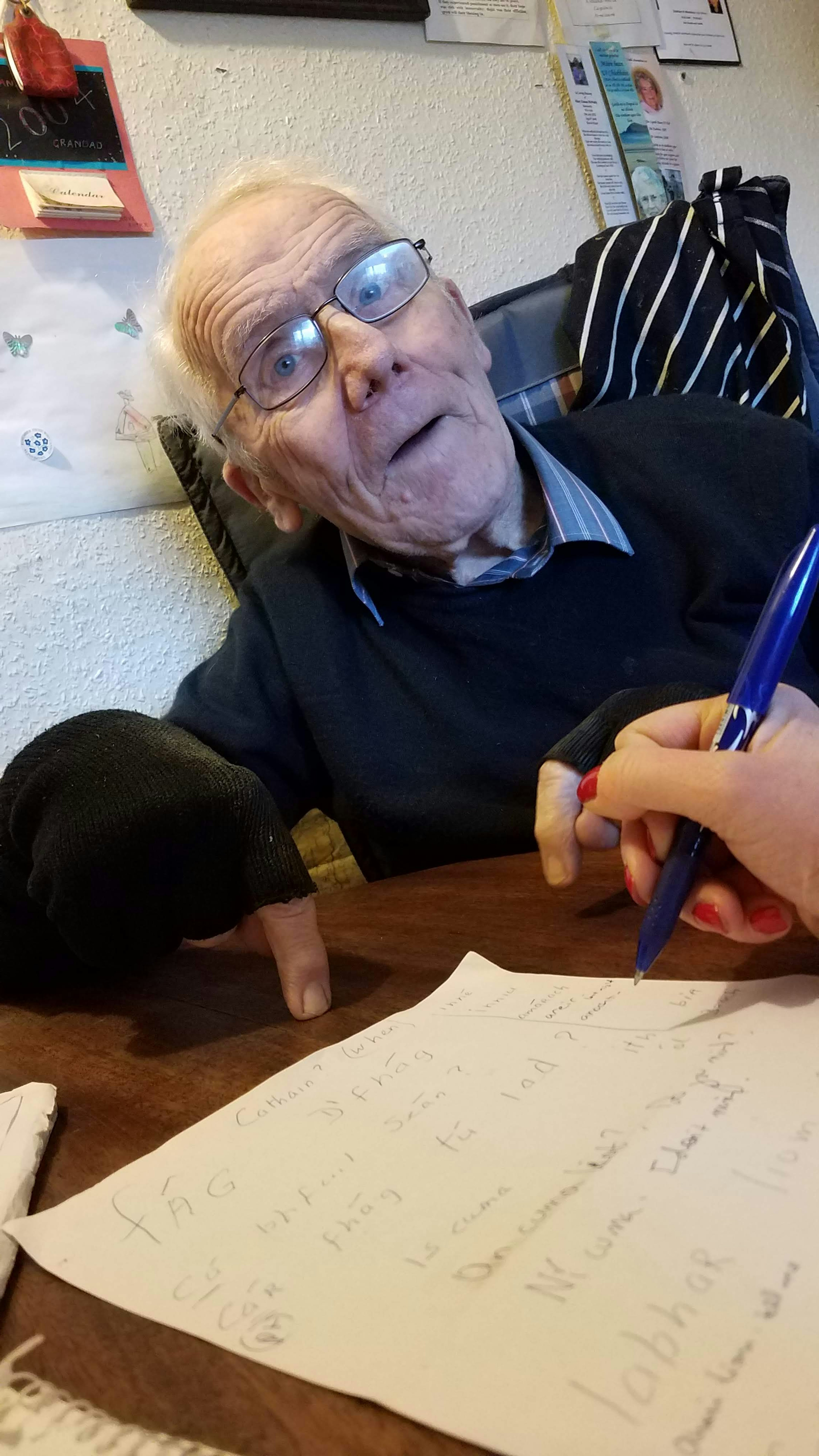 Kerry writes her Gaelic lesson as Donal, her tutor, looks on and points on the table for emphasis