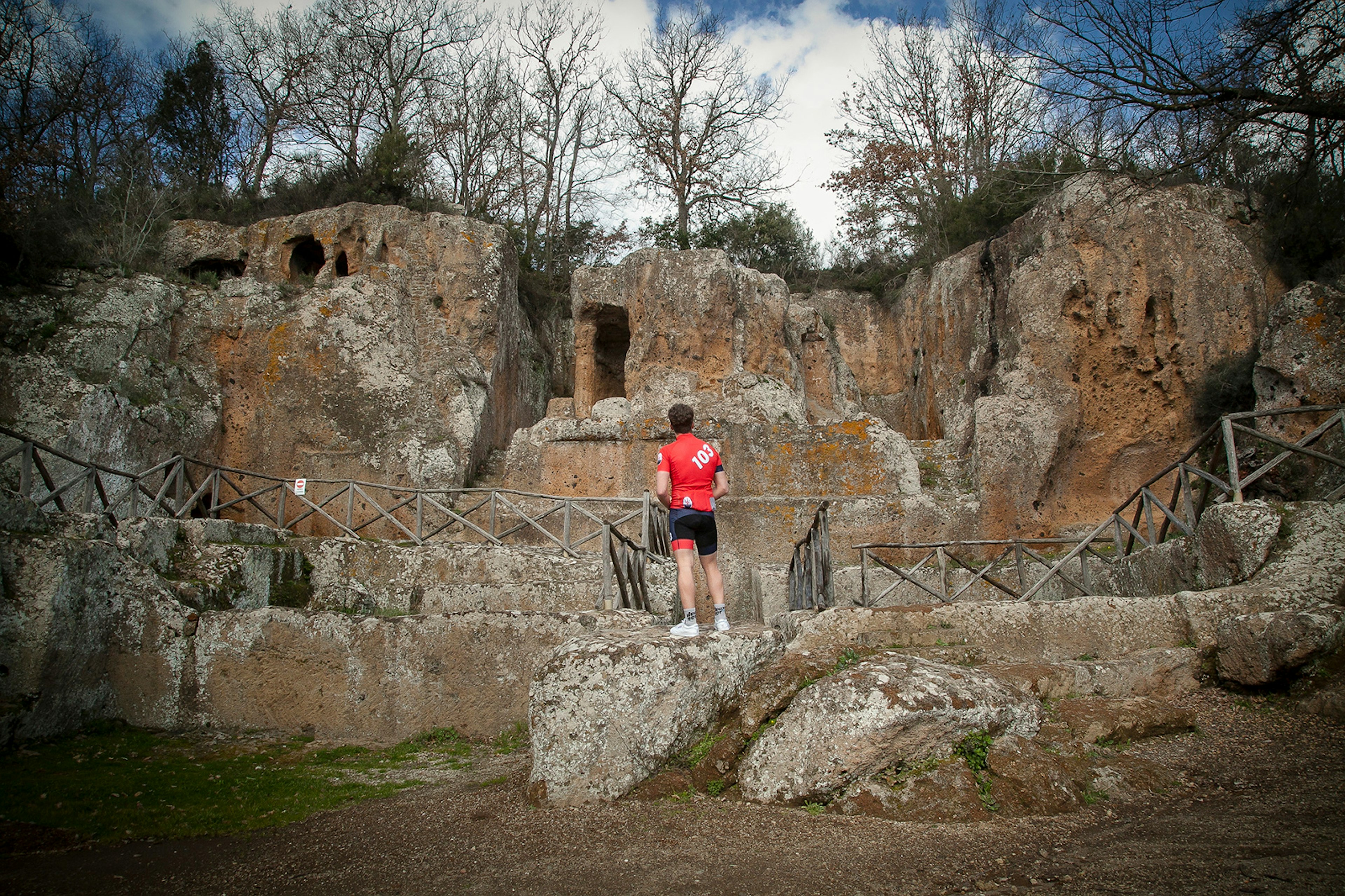 A cyclist stands atop a rock platform looking at rudamentary dwellings hewn from the rock © Mario Llorca / mariollorca.com