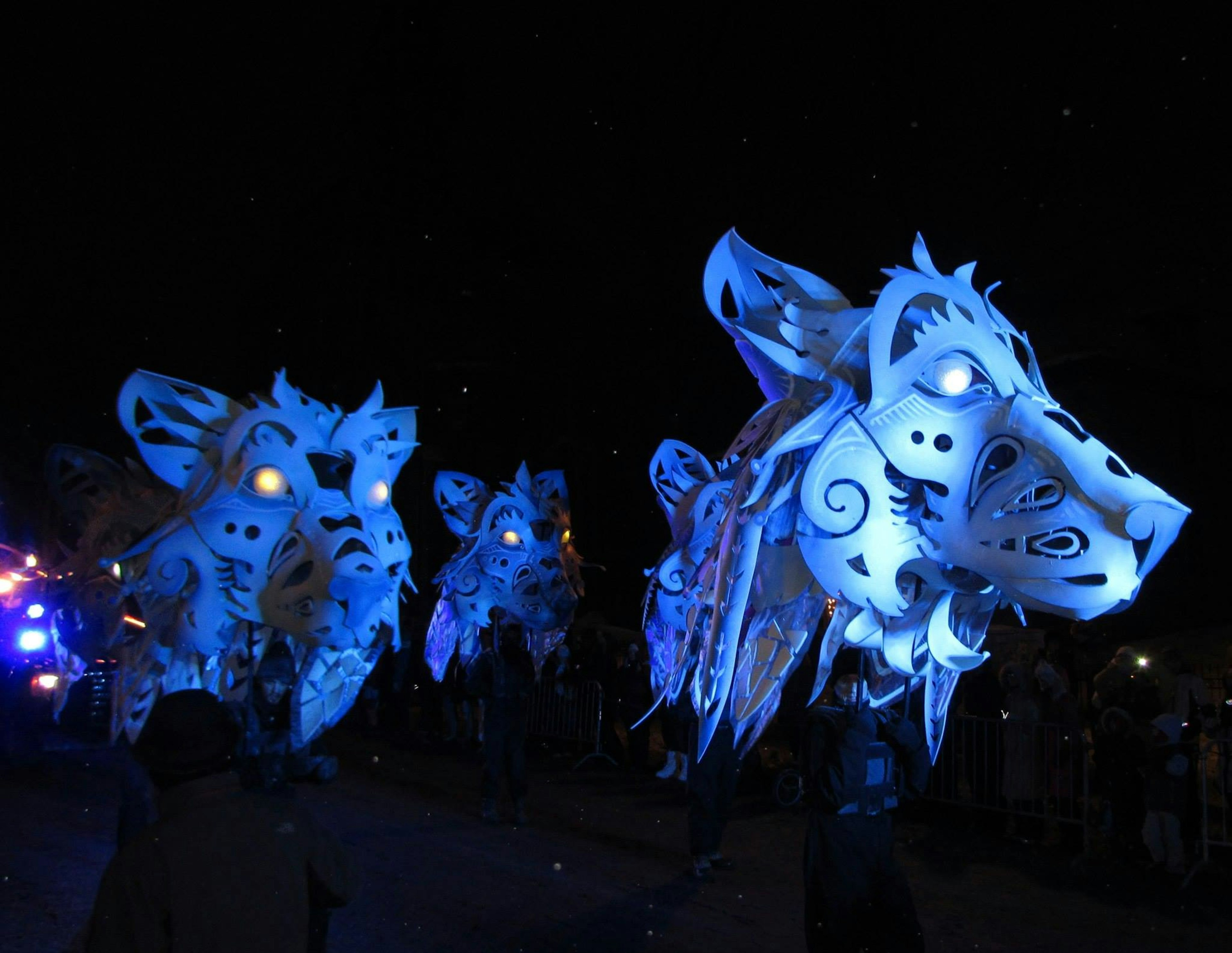 Very large, decorative white wolf heads are carried through a crown in a night scene in ϳé City.