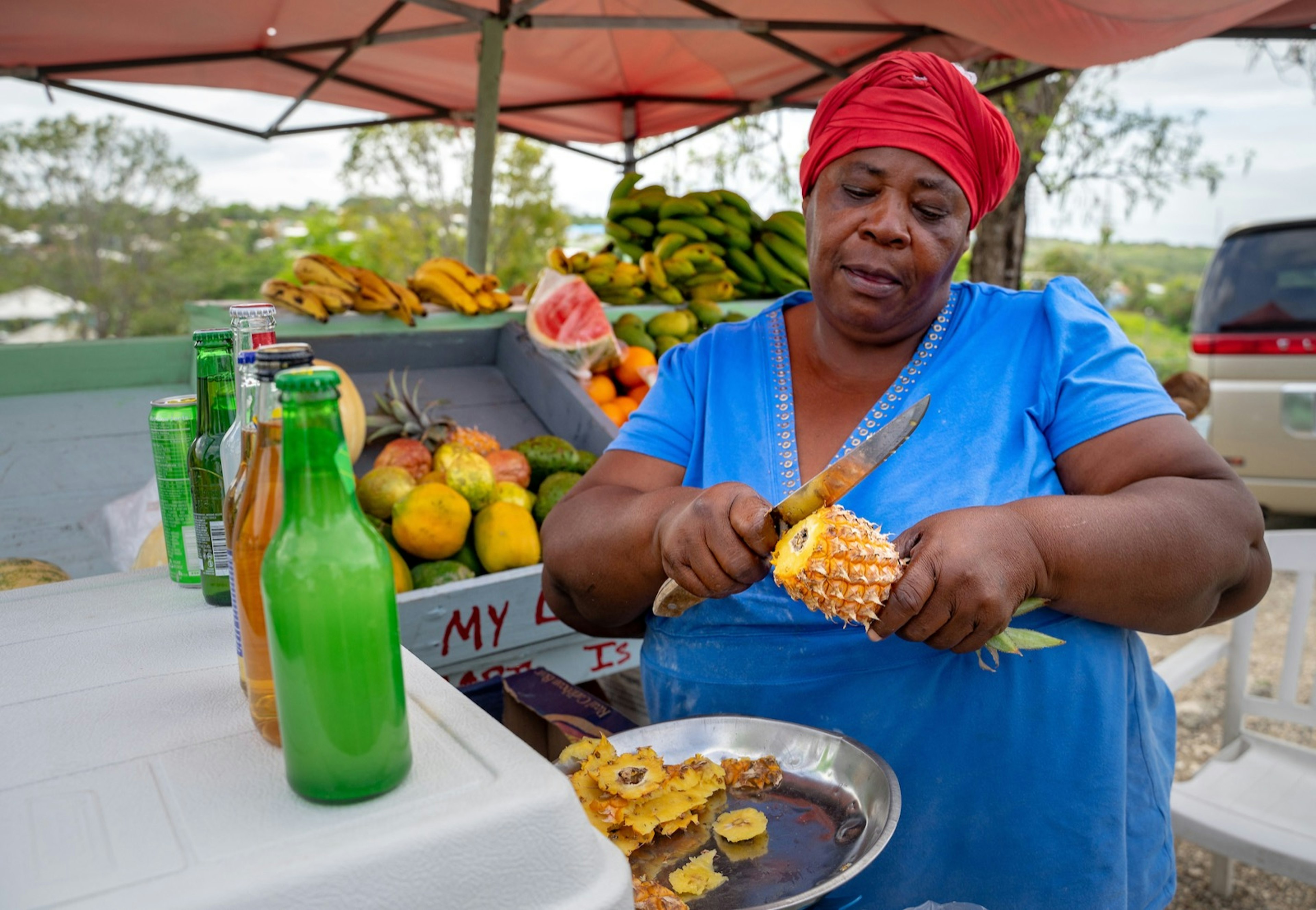 A woman chops a pineapple into a frying pan inside a fruit stall in Antigua and Barbuda.