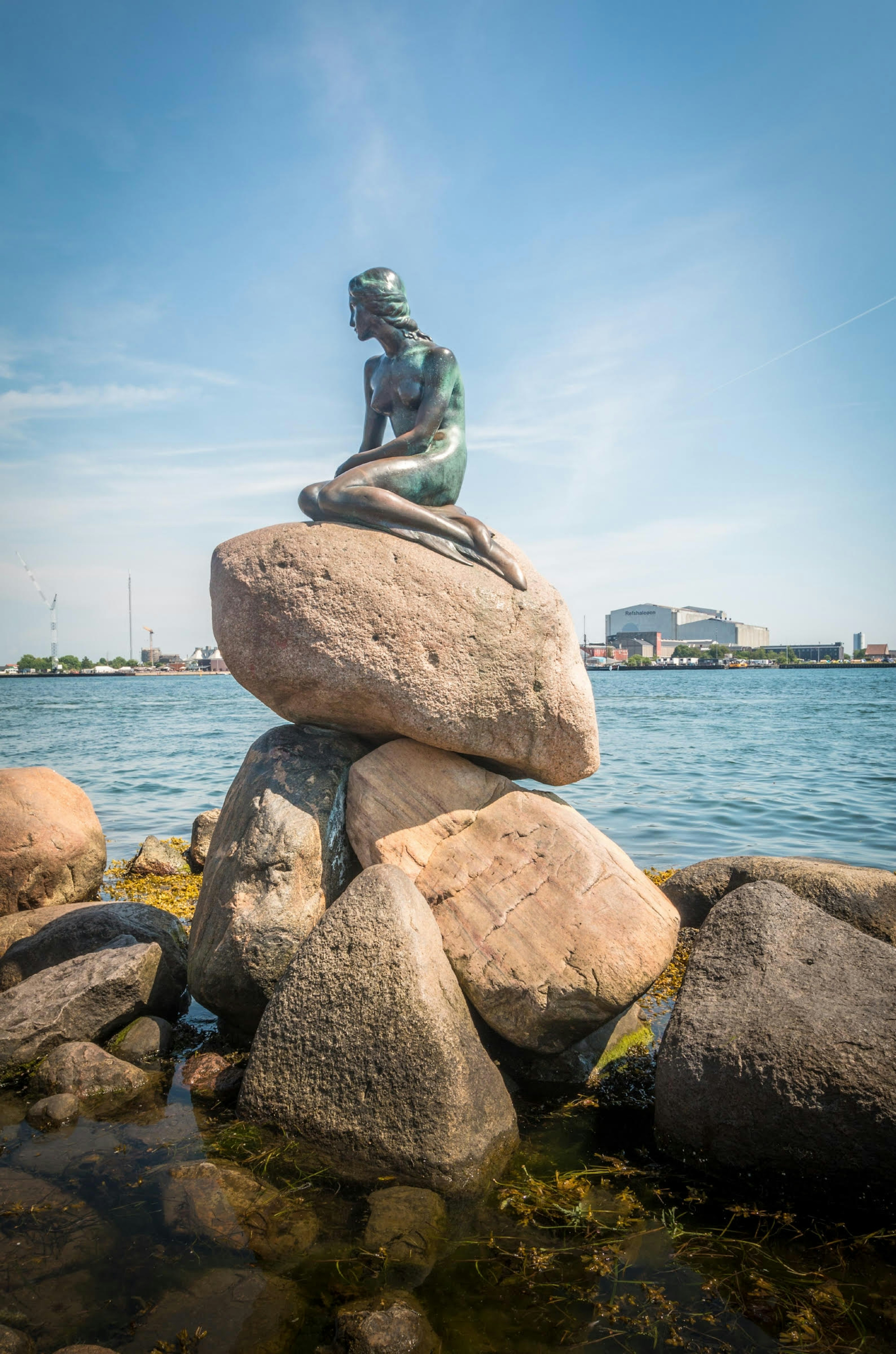 Statue of the little mermaid on top of a rock, beside the sea, in Copenhagen.