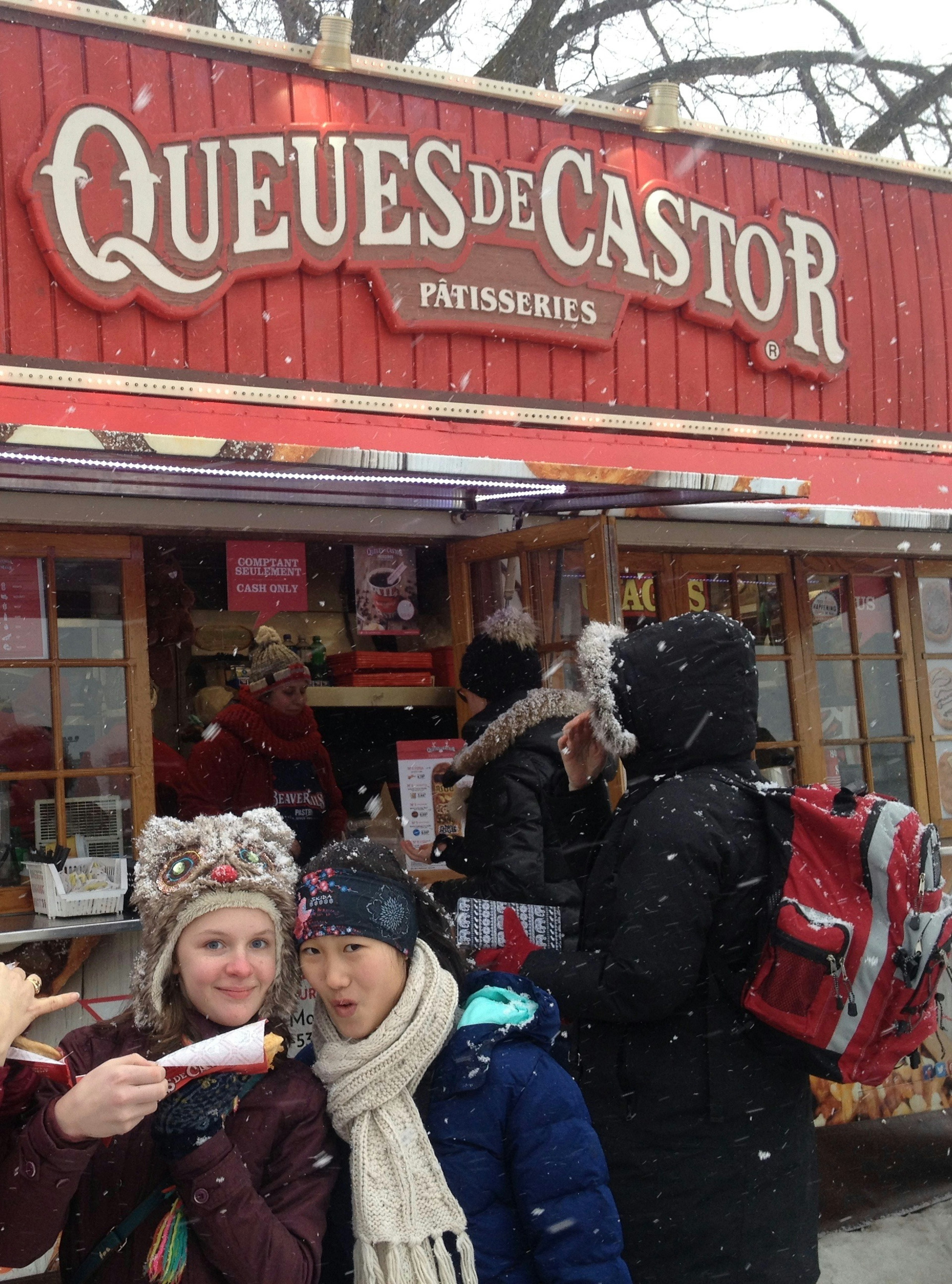 Two young women eat a doughy confection in front of a store in ϳé City.