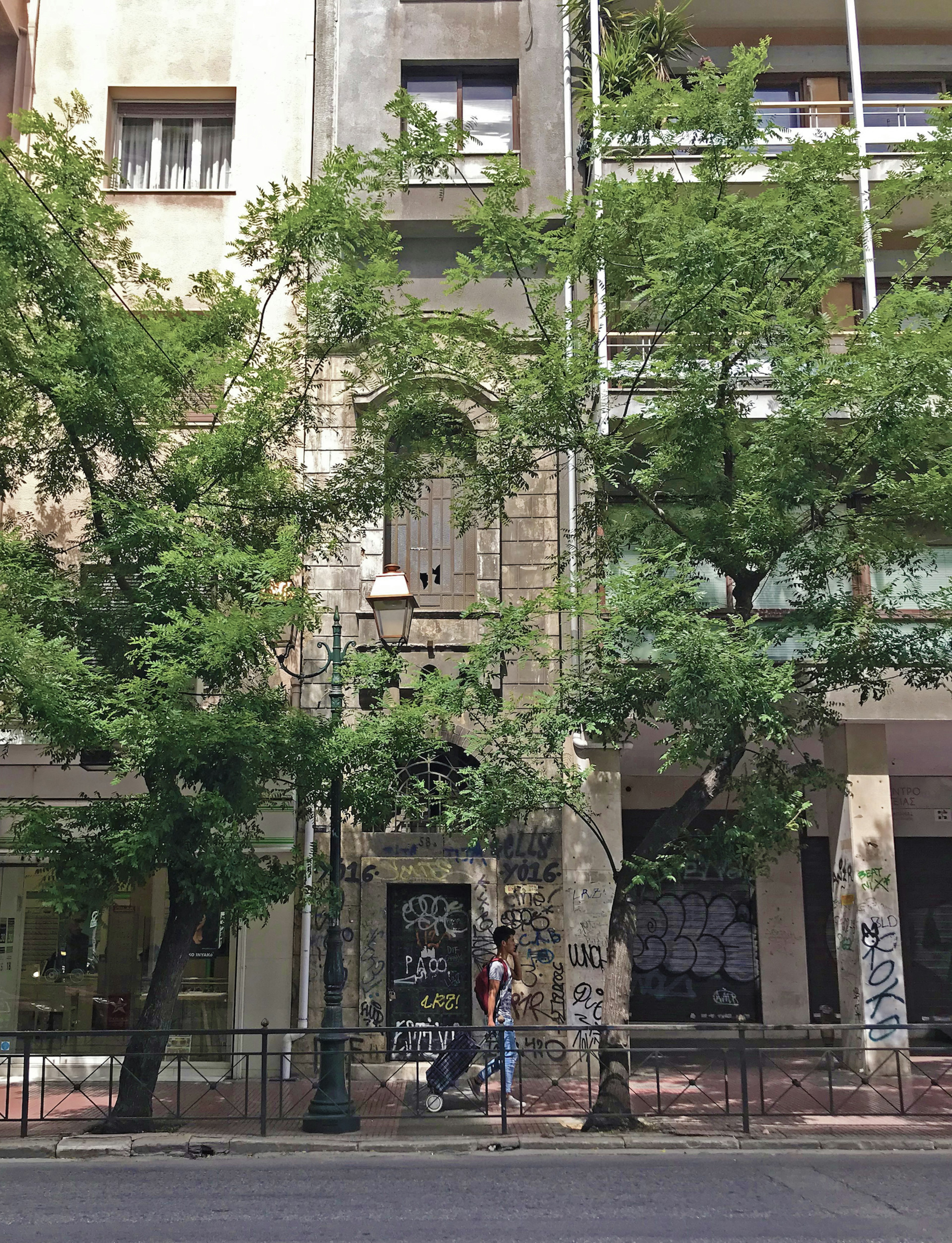 A concrete building with two trees and a person walking in front. The building was rumoured to house Satanic rituals.