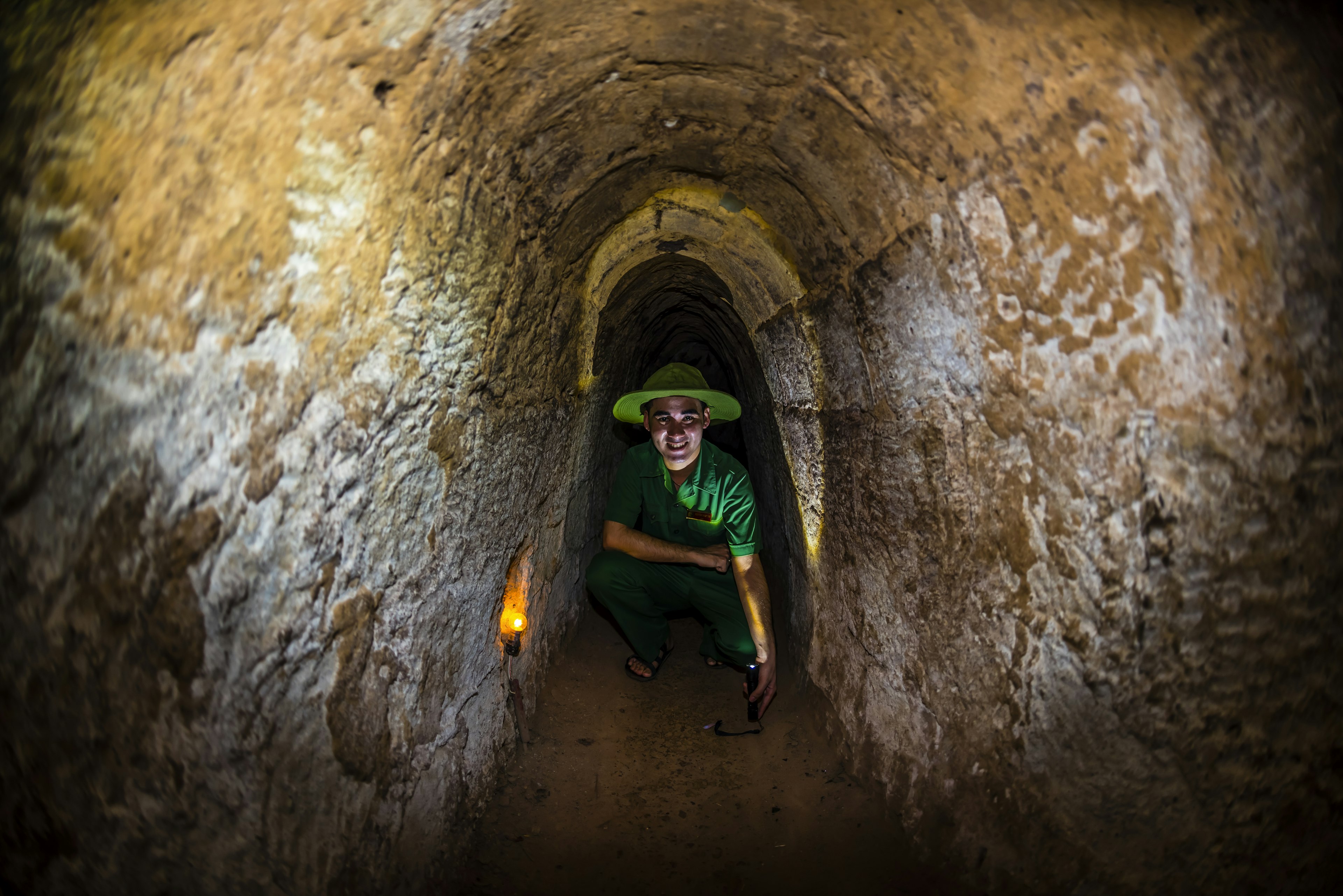 A bright image of a man wearing green in the Cu Chi tunnels.