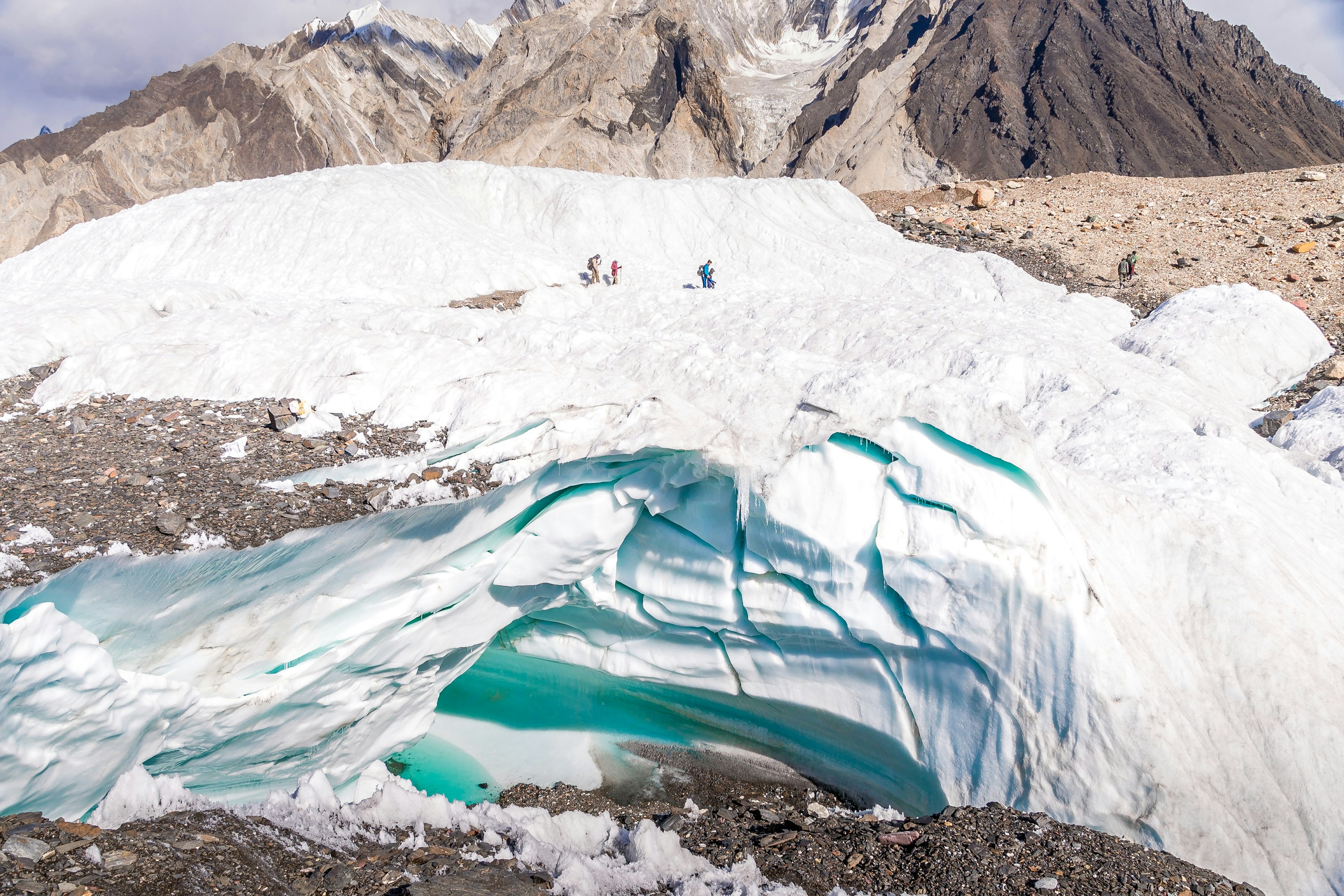 Peter hikes through an ice field en route to K2 base camp. The climbers appear tiny against the white backdrop of the ice. In the background mountain peaks are visible.