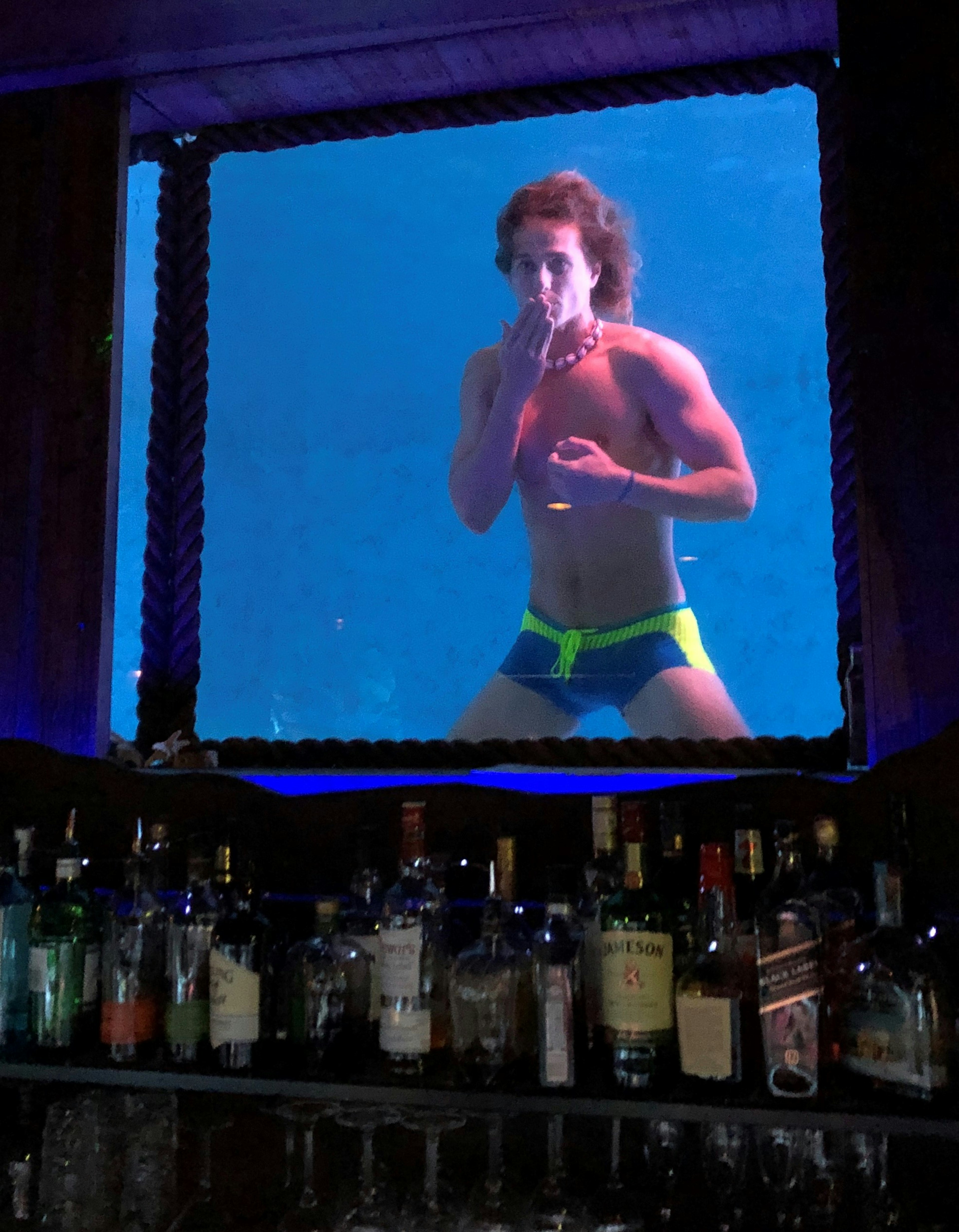 A man wearing a tiny speedo looks through an underwater porthole at the Wreck Bar in Fort Lauderdale.