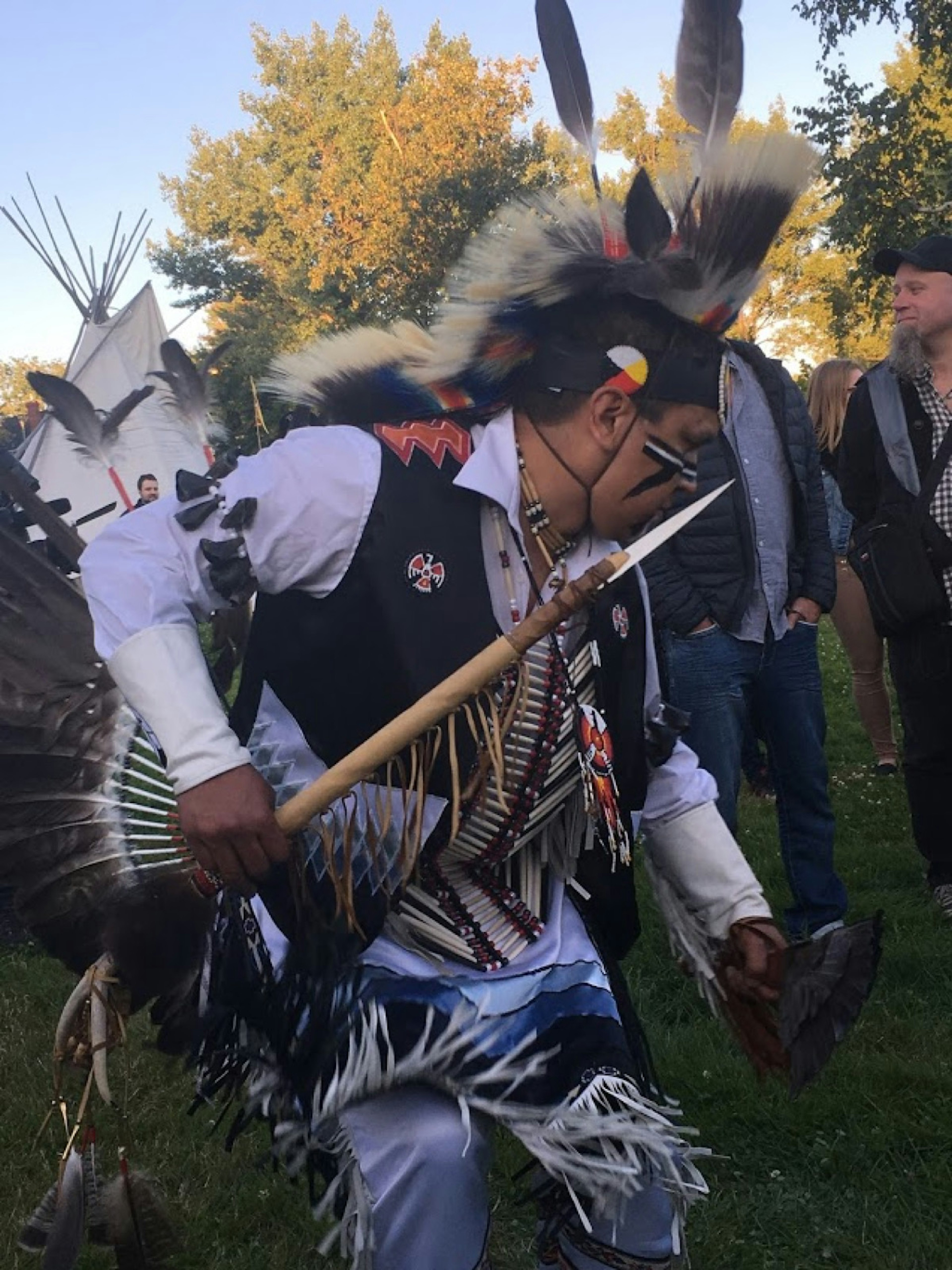 An indigenous dancer with beads, feathers and a pointed stick dances with a crowd around him @ Fiona Tapp / Lonely Planet