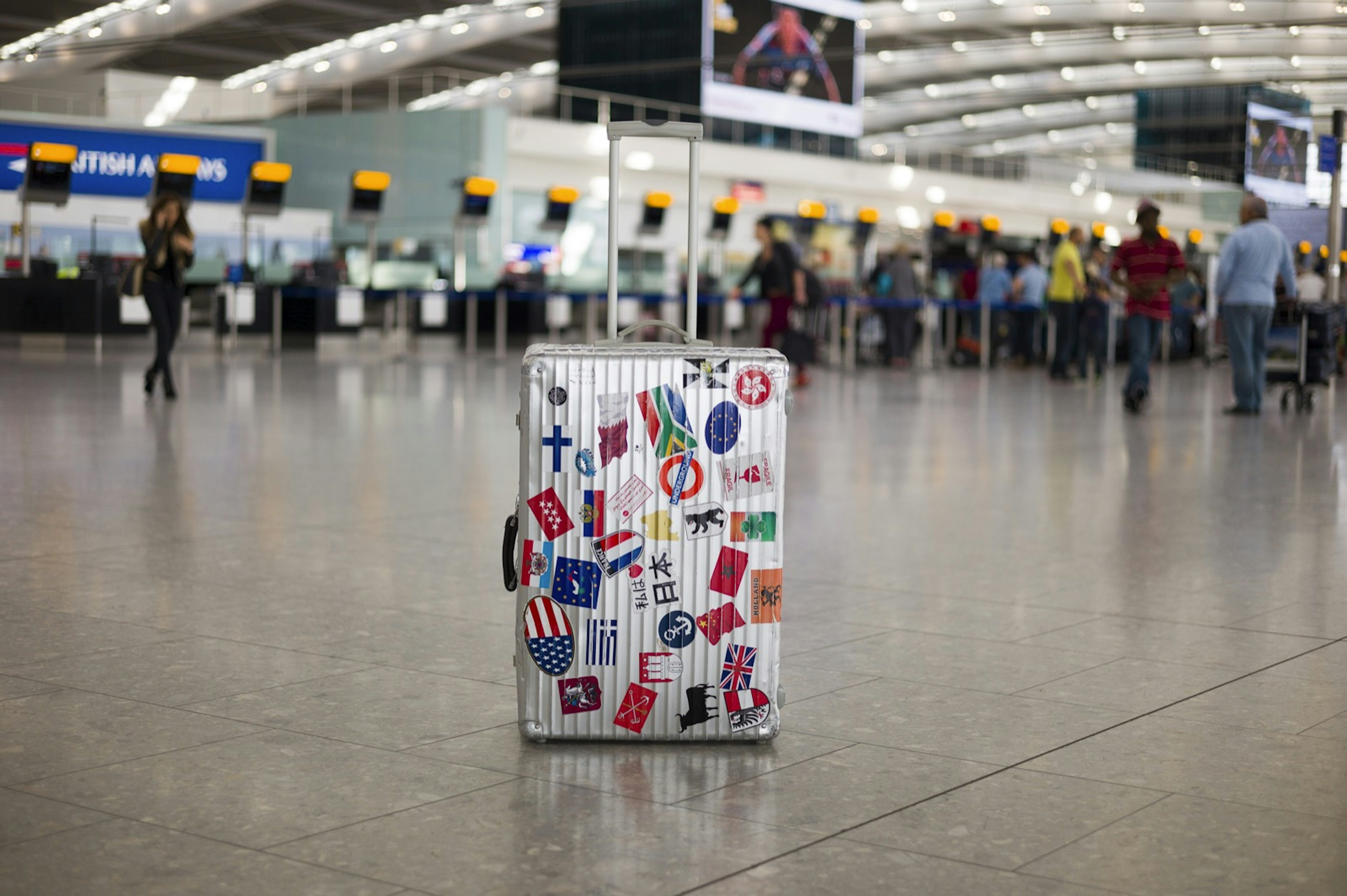 A suitcase full of stickers of various countries sits in an airport departure area. $125 travel ideas