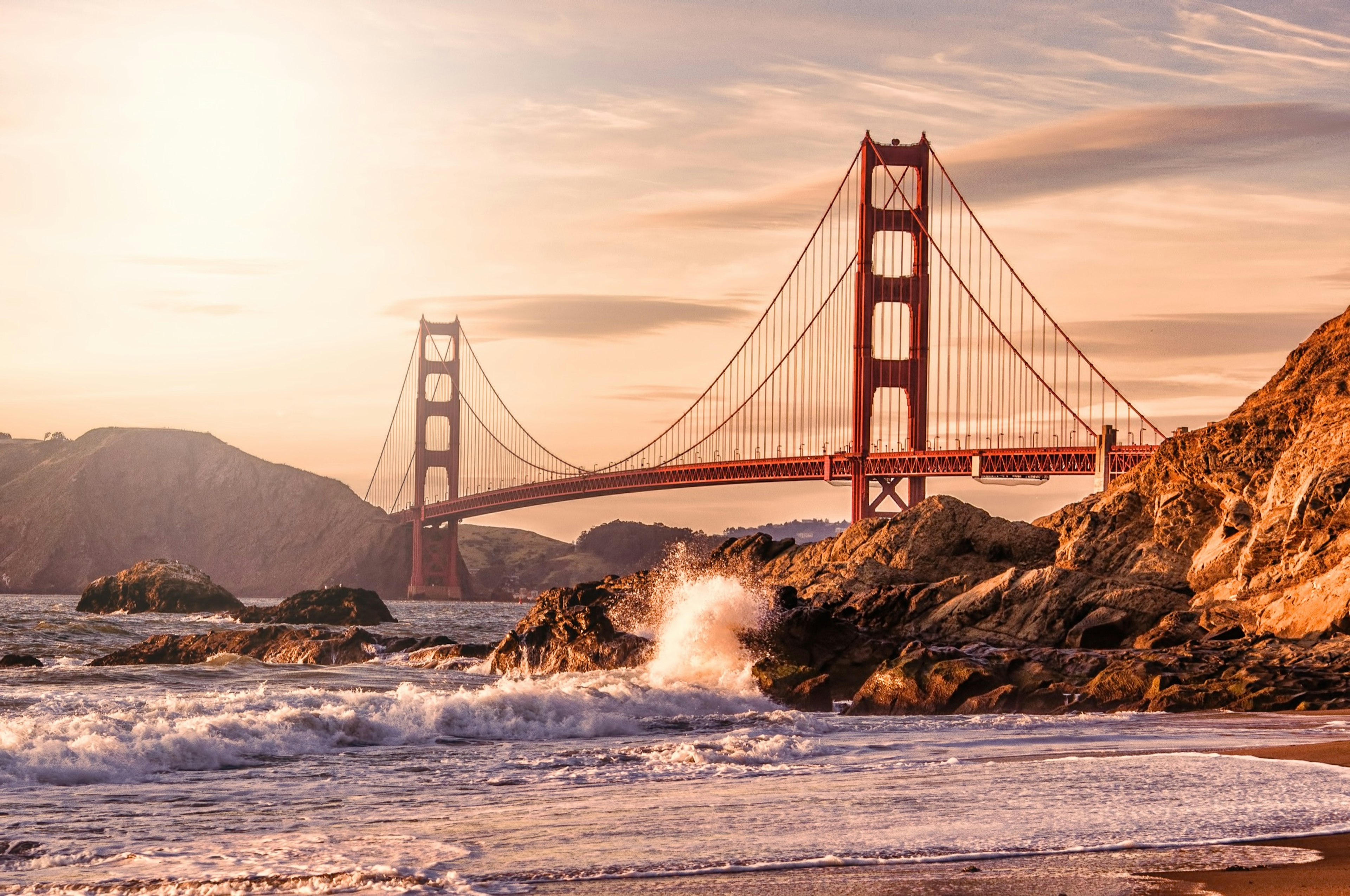 Waves lap the bank of San Francisco Bay as the orange-red span of the Golden Gate Bridge stretches across above to the opposite bank; Best American architecture