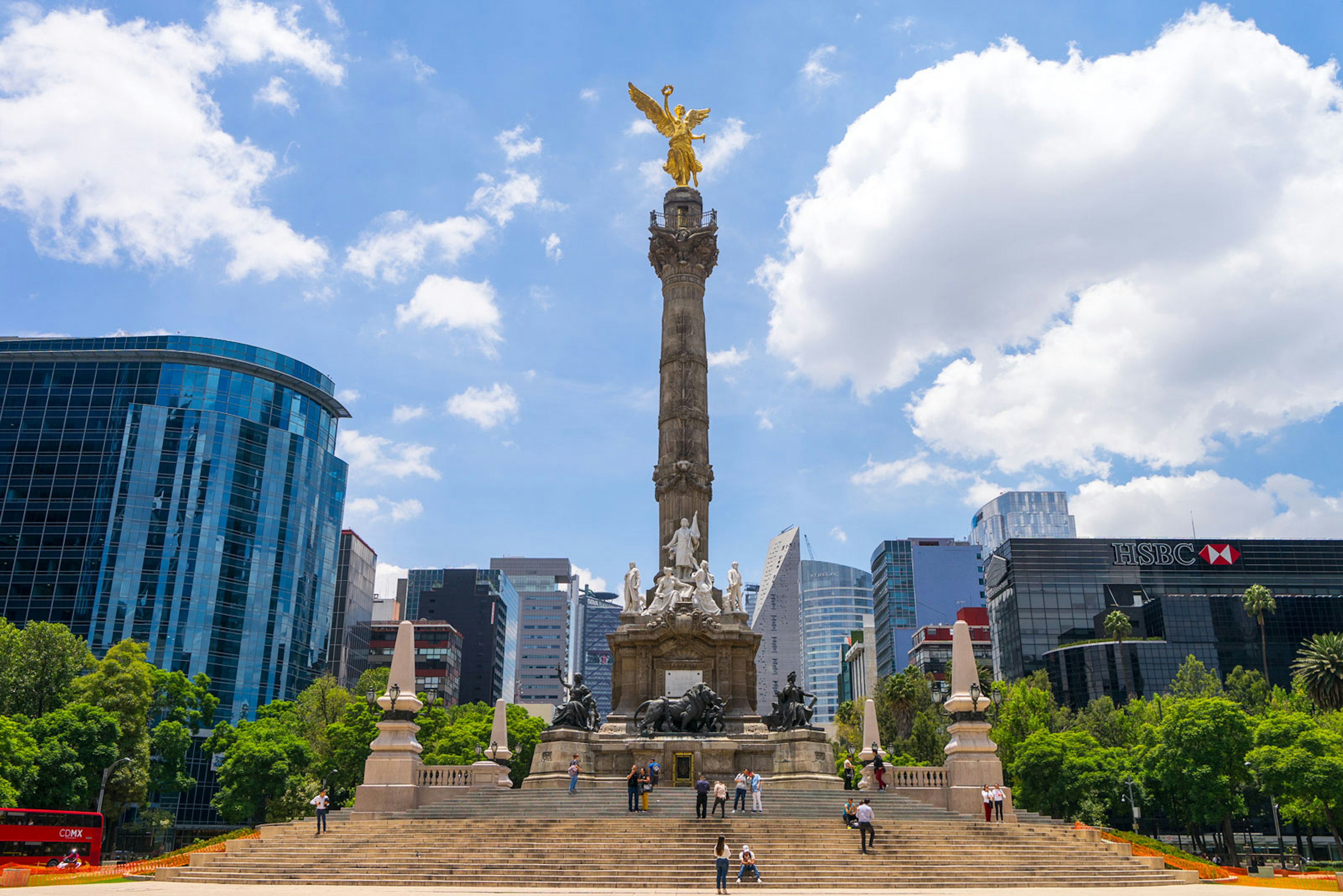 an obelisk topped with a golden angel stands surrounded by high rises