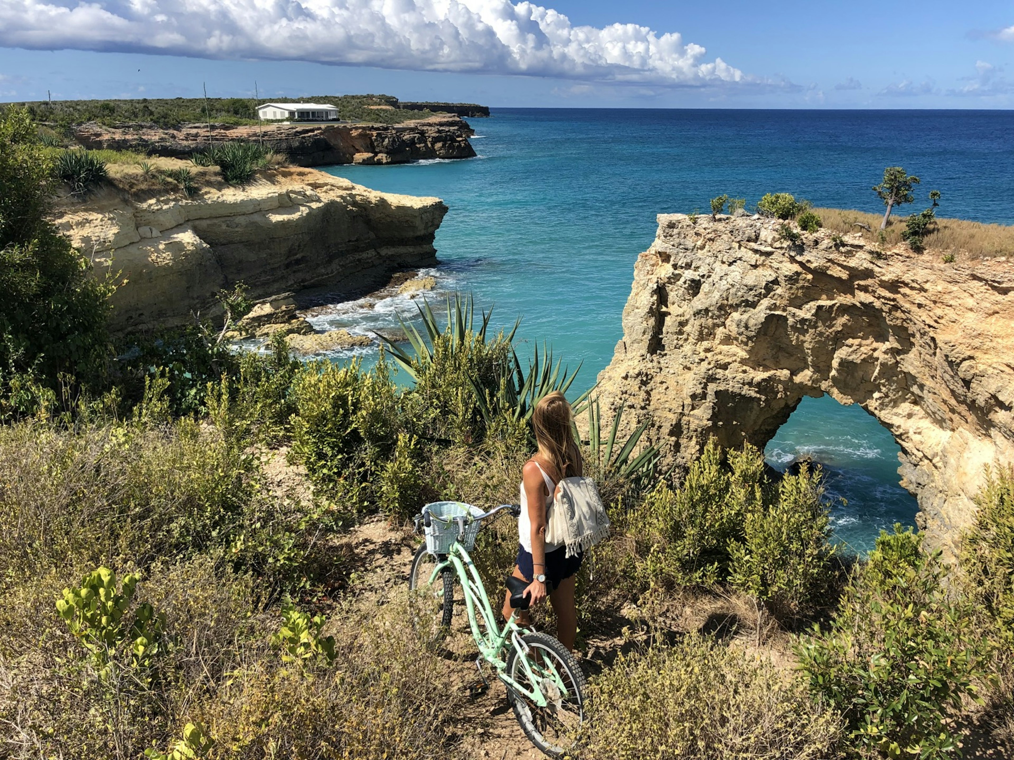 A woman with a bike stands stands on edge overlooking The Arch on the West End on Anguilla