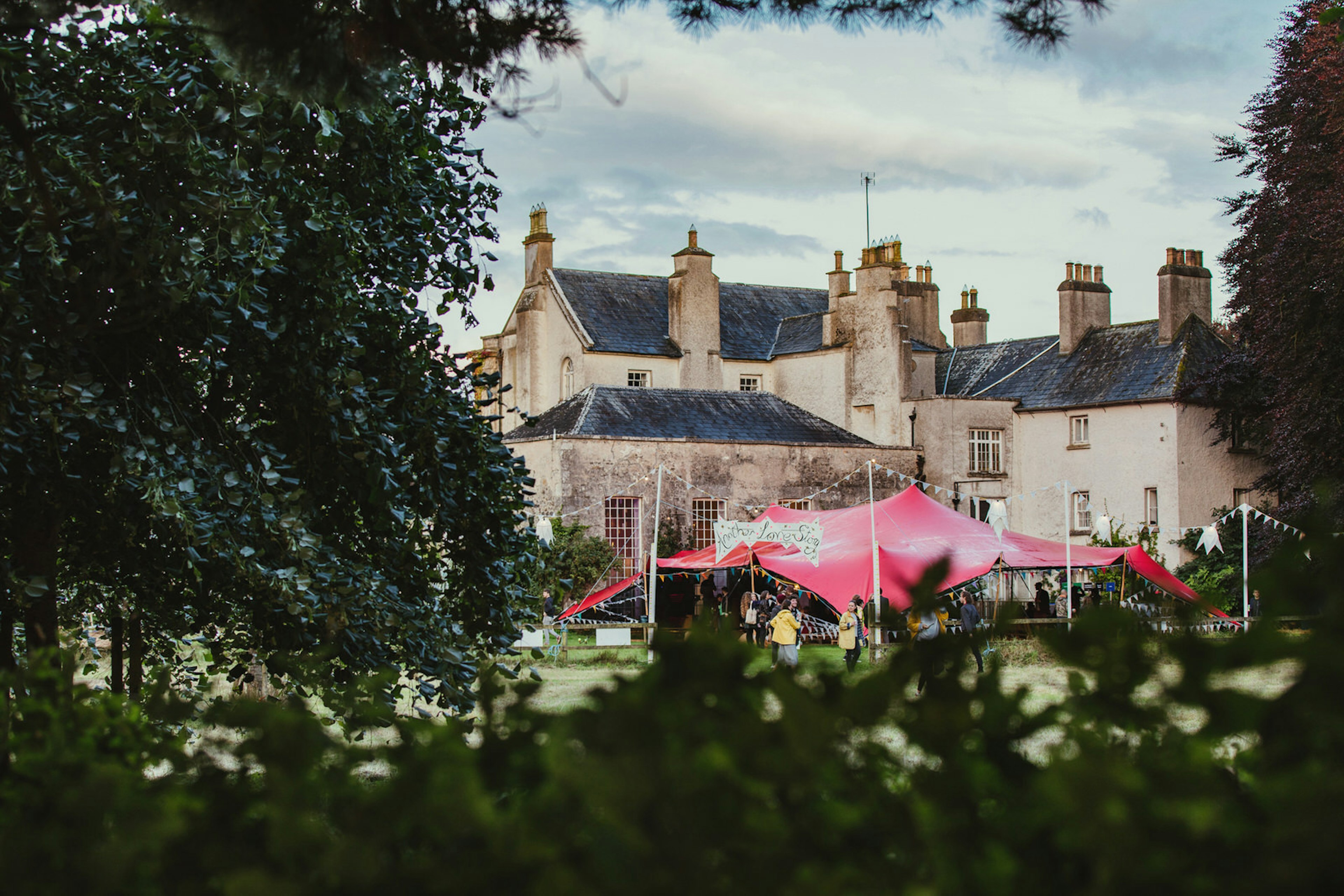 Europe music festival - a pink canopy and grand house peak out from behind a leafy green forest © Another Love Story