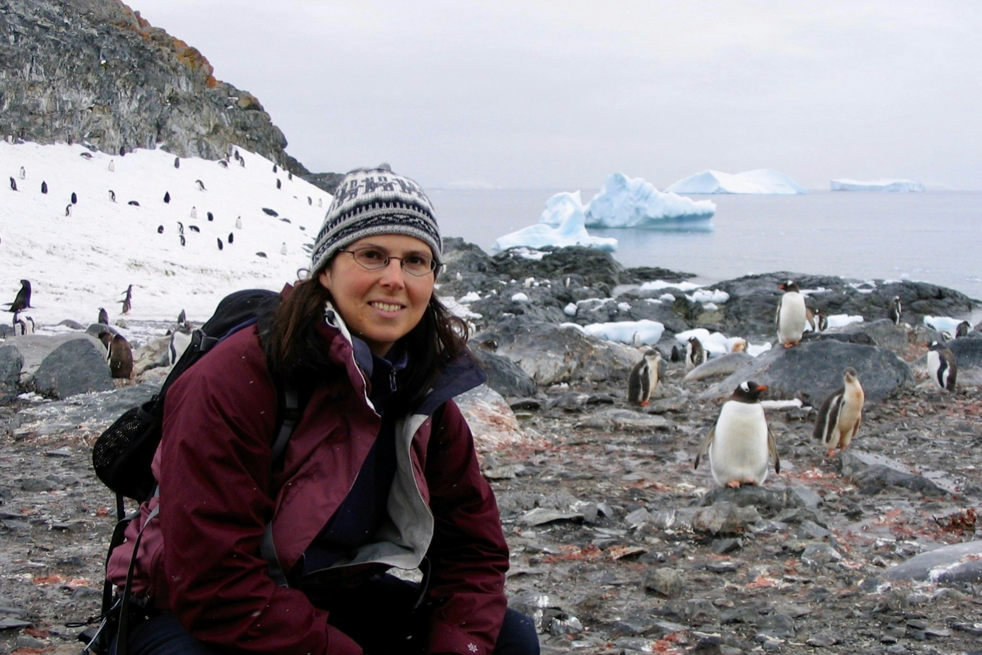 Marie-France poses next to some penguins near the coastline in Antarctica