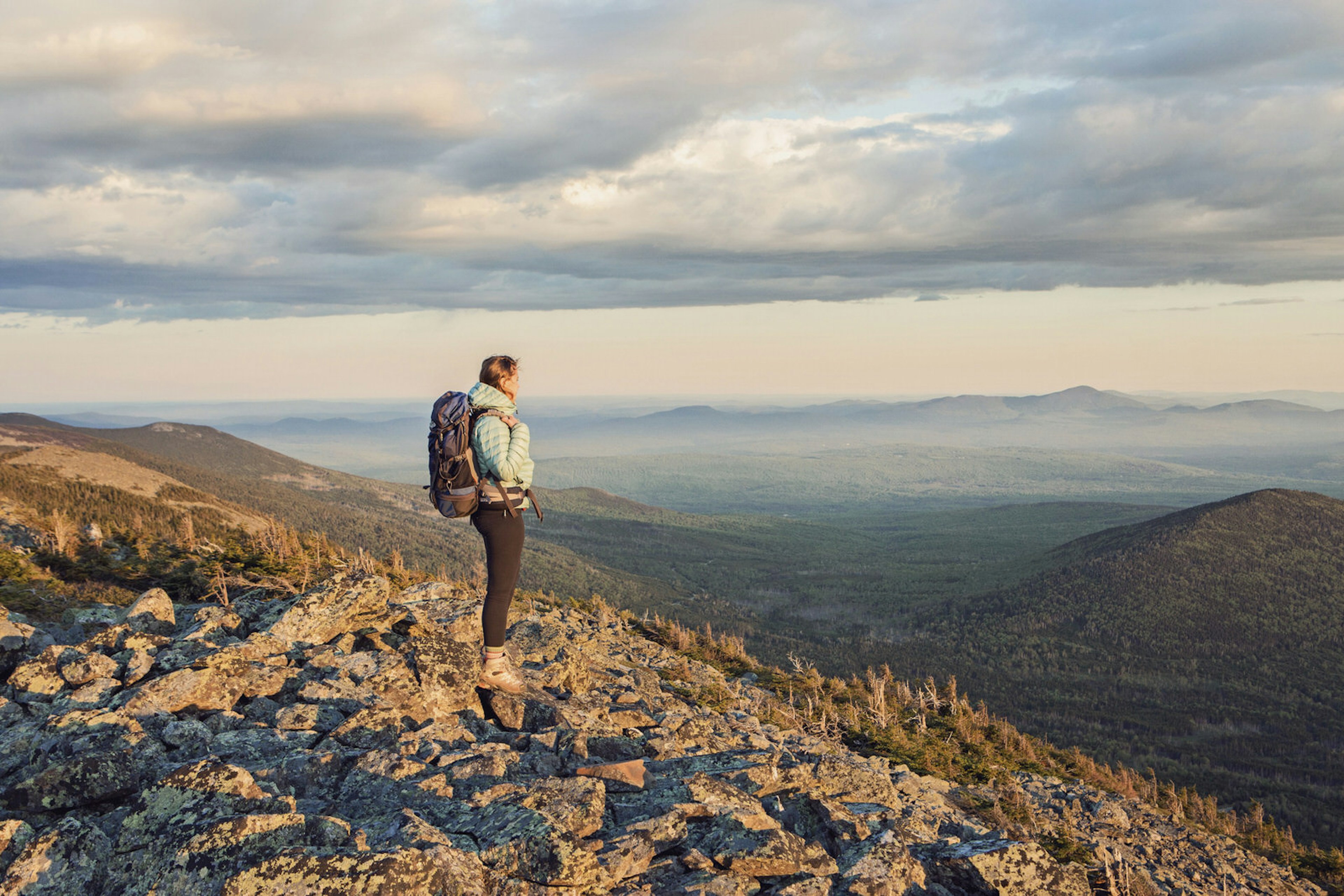 A young woman stands at the top of Mount Abraham, along the Appalachian Trail in Maine's western mountains on an overcast day