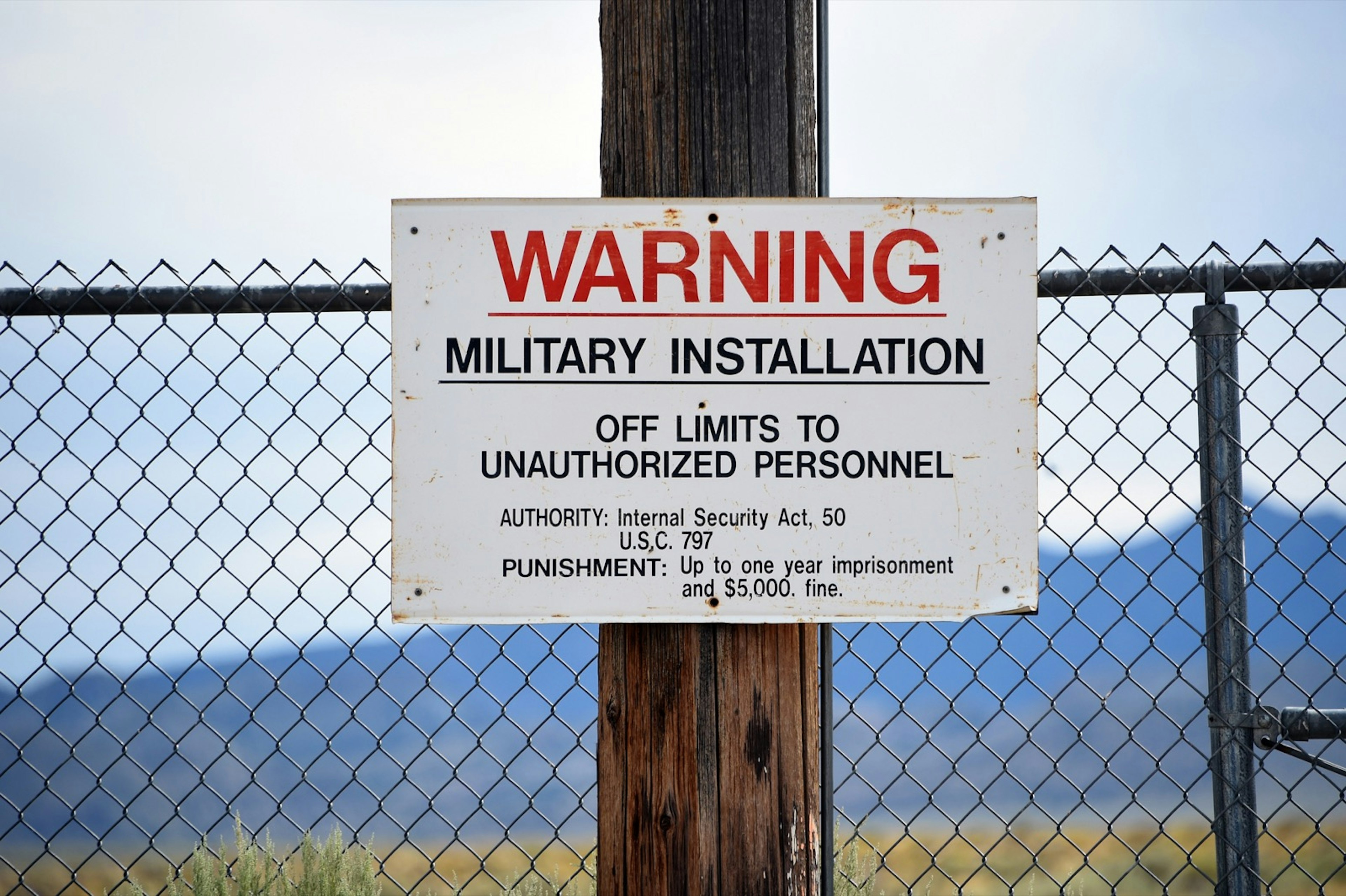 A sign warning of against unauthorized trespassing hands on a wooden post in front of a chain-linked fence near Area 51