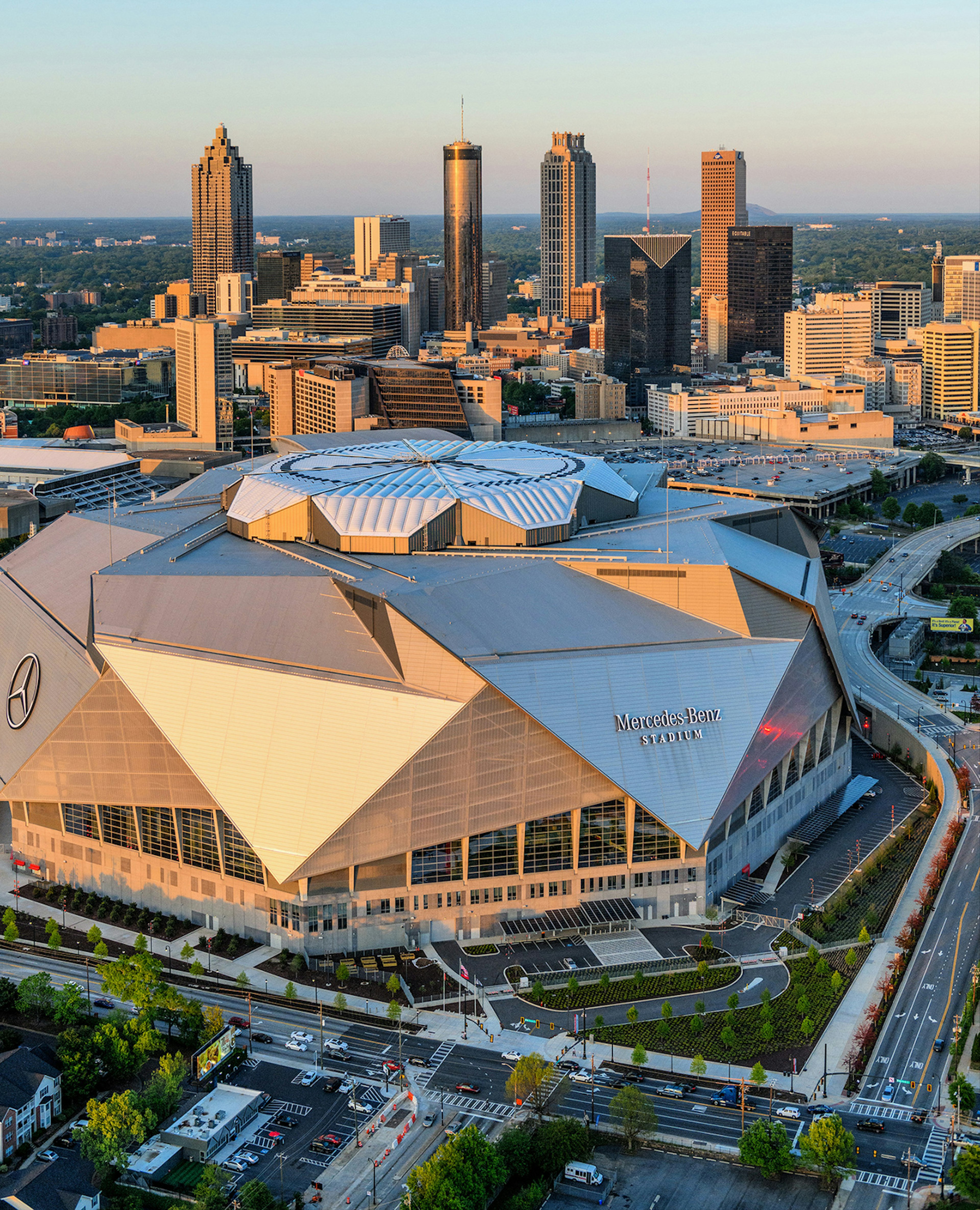 Sun glints off the multifaceted dome of the new Mercedes Benz Stadium in Atlanta, with the skyline behind it at sunset