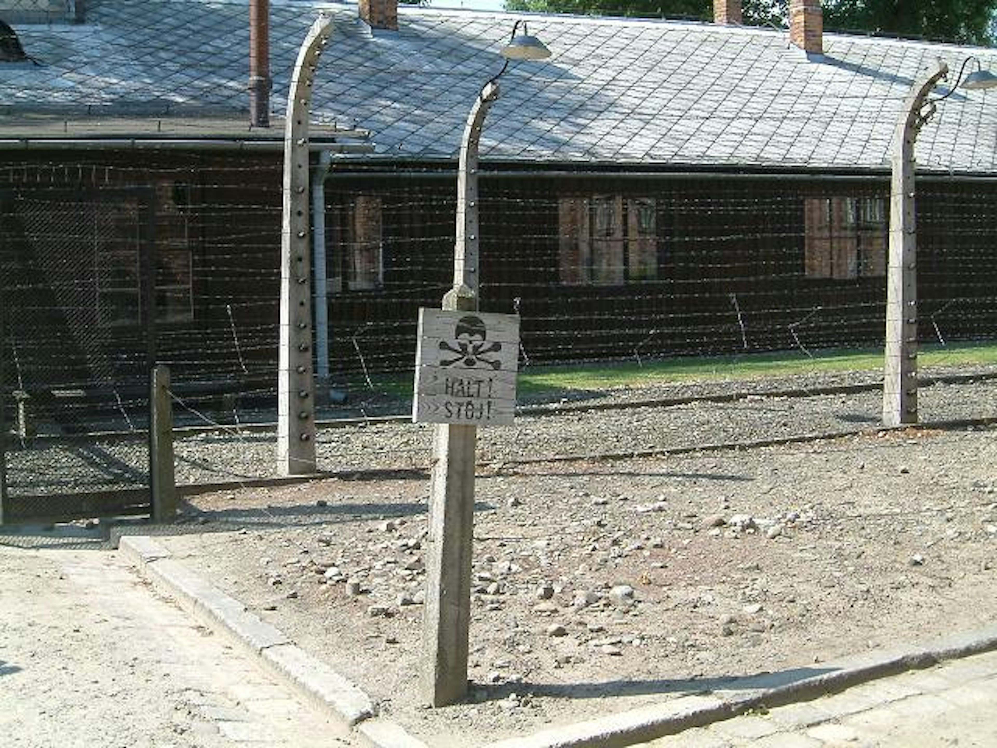 A sign with a skull and crossbones stands between two sets of wire fencing. The text says