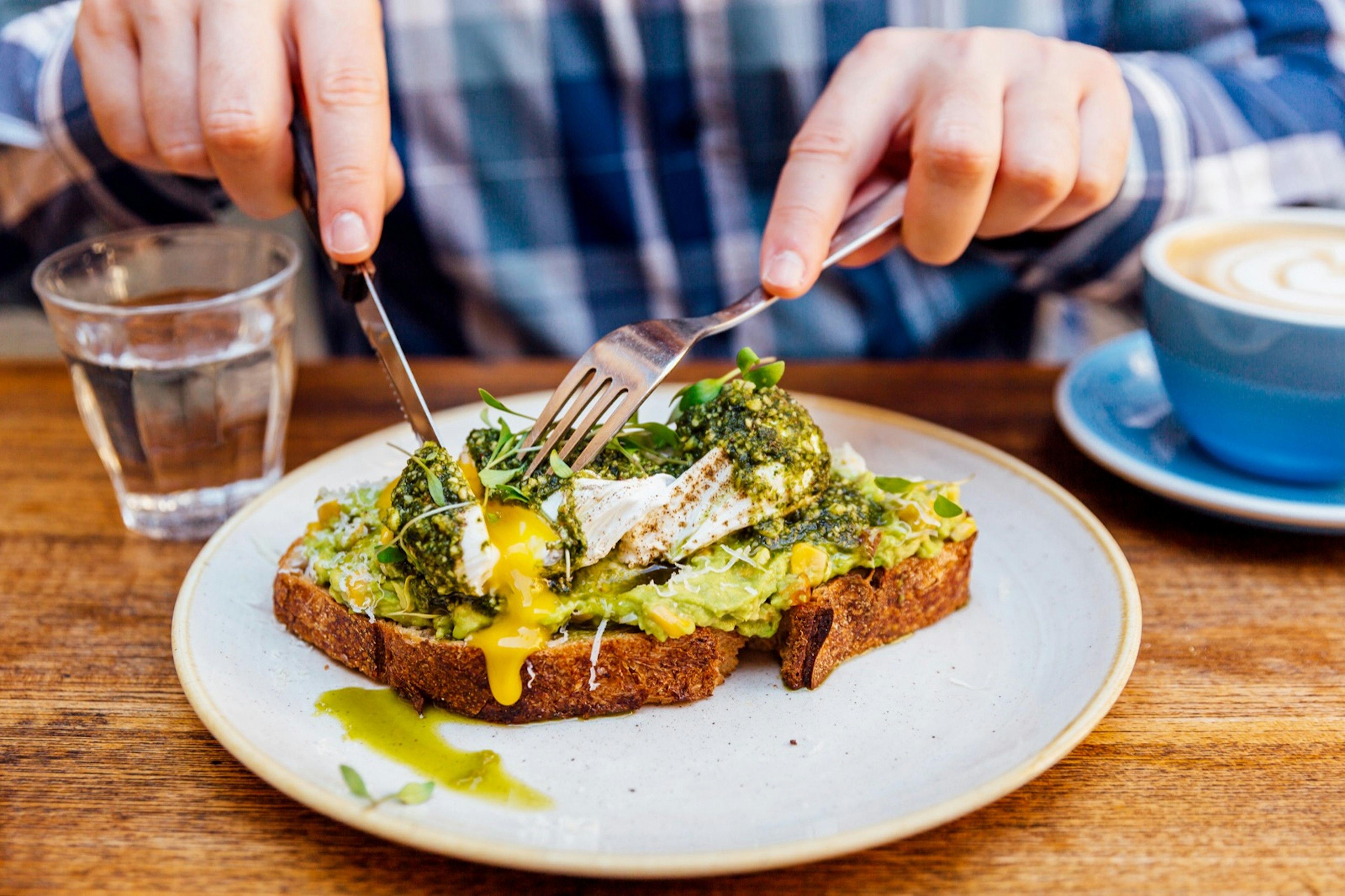 Man cuts into avocado toast with an egg on it