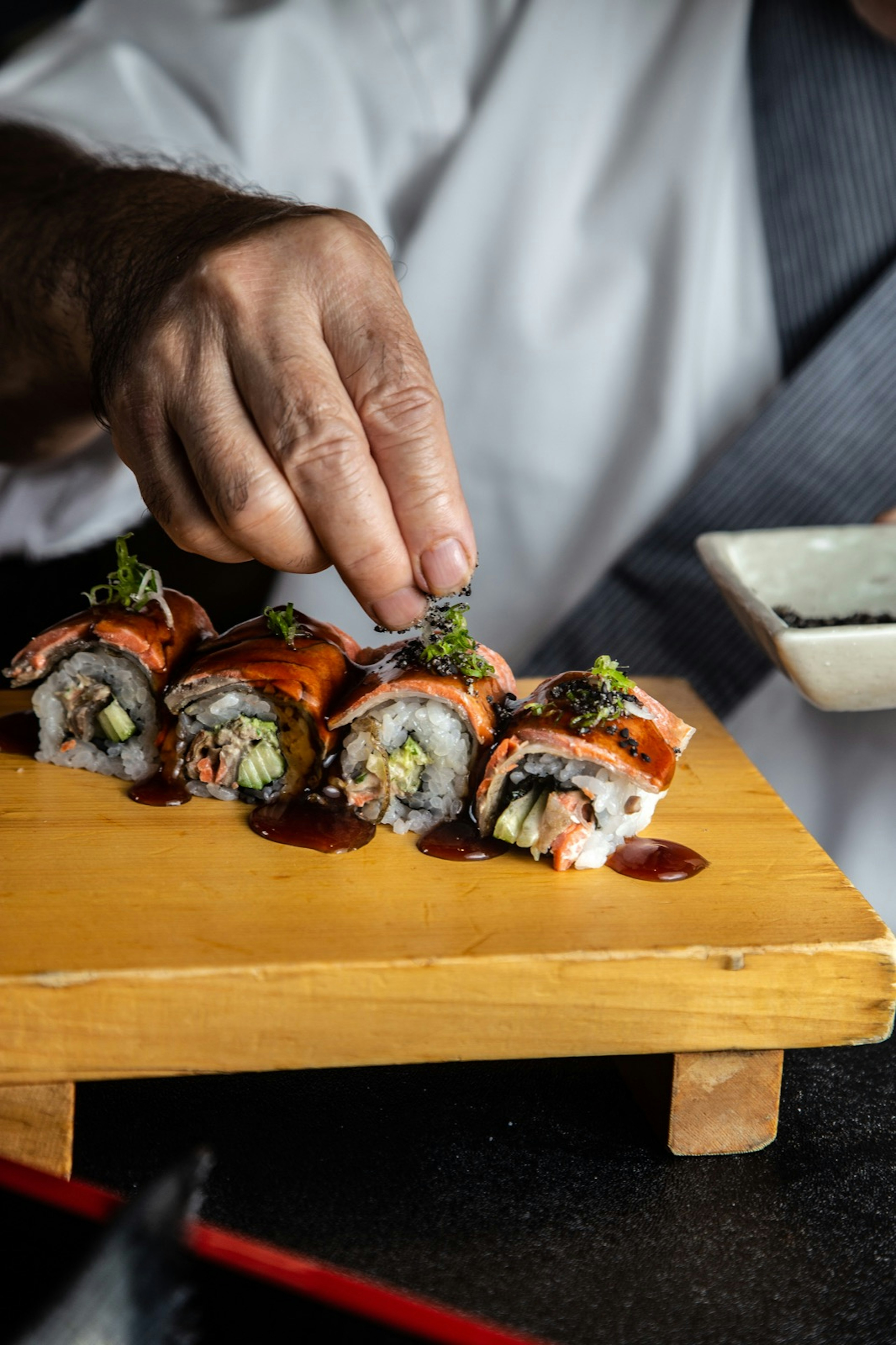 A chef's hand adding ingredients to a BC roll on a wooden cutting board; California roll