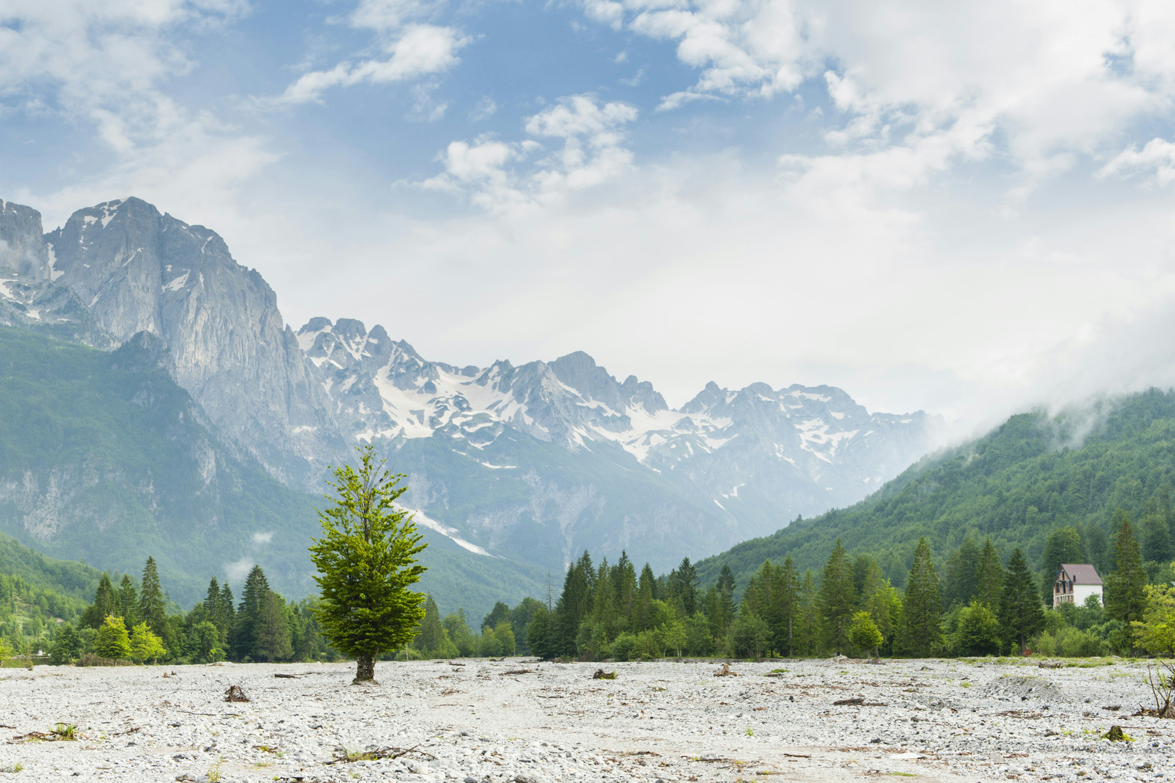 A wide gravel bed is spread between forested mountainsides at Valbonë