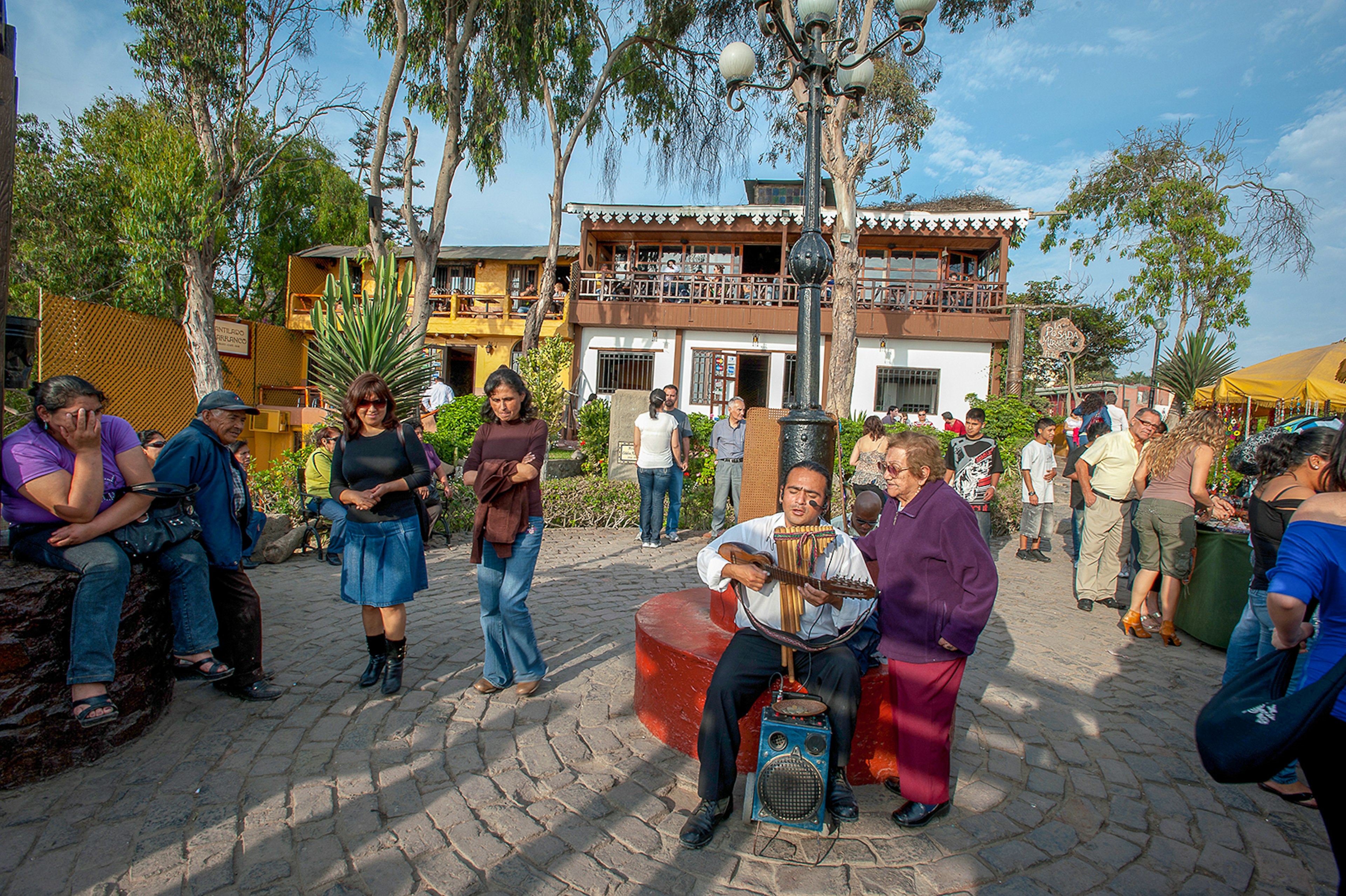 man plays music in a cobblestone square while people listen