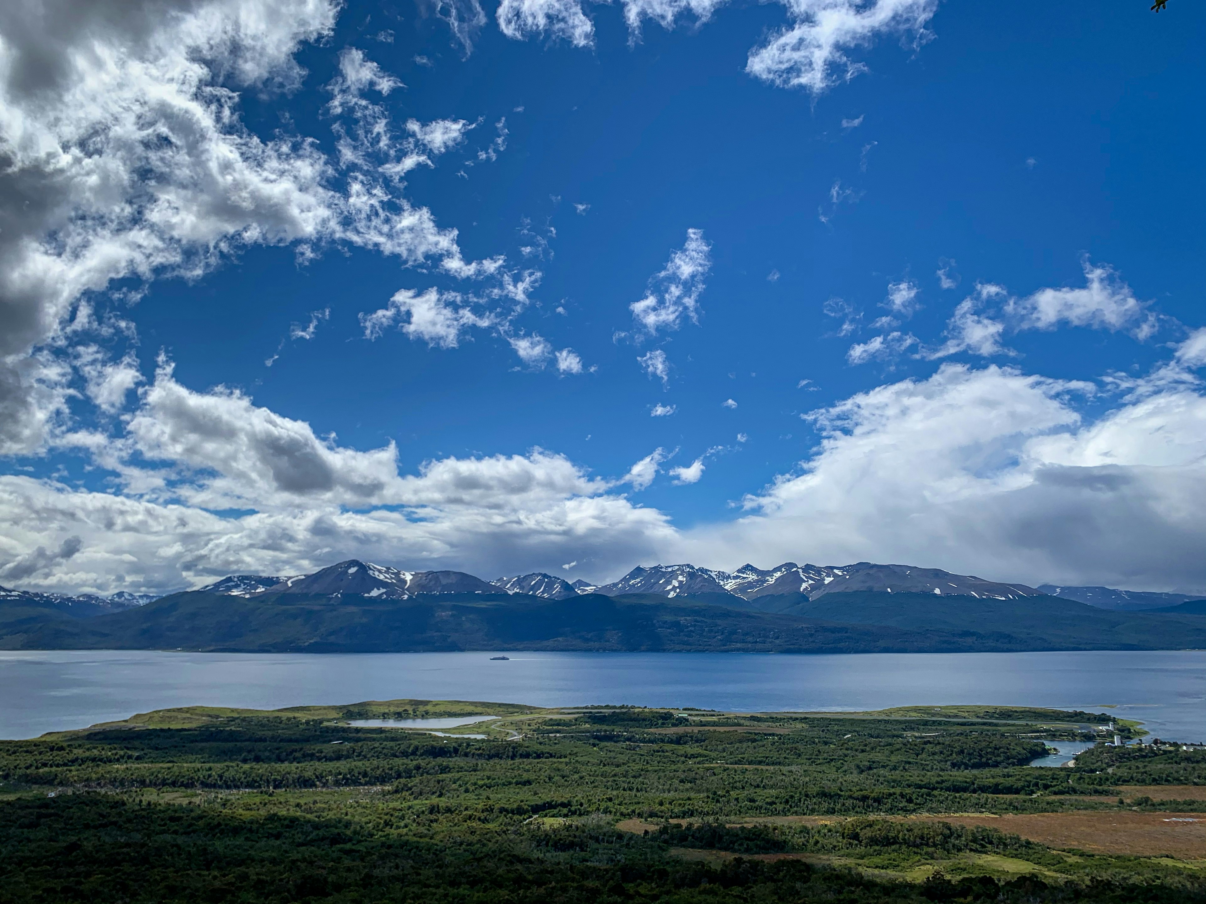 A flat, tree-covered piece of land is separated from a mountain range by a wide body of water, the Beagle Channel.