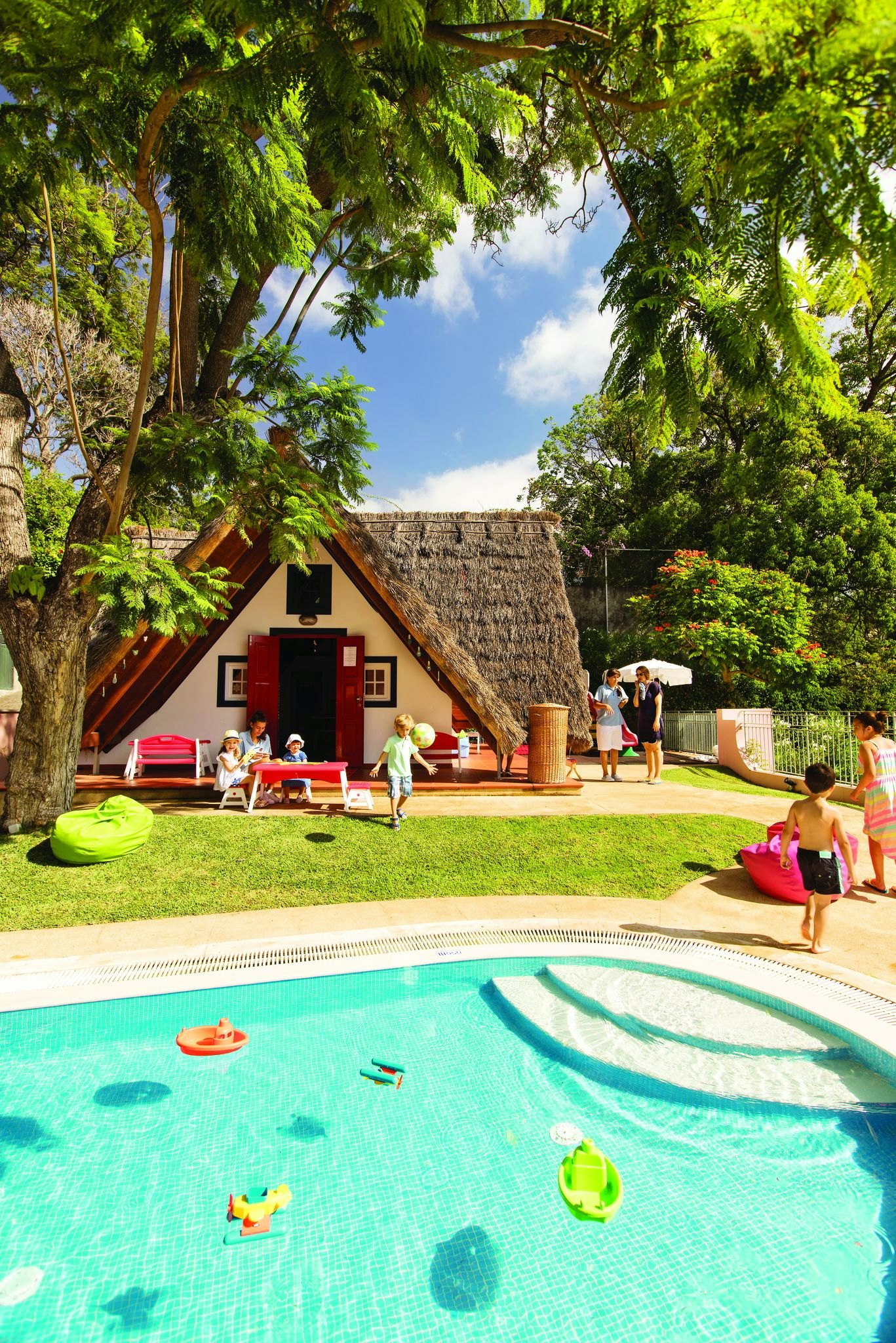 A small, thatched house by a pool at Belmond Reid's Palace, Portugal, pictured on a sunny day. A family can be seen sitting outside.