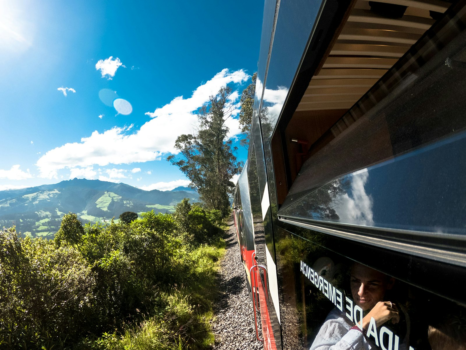 A photo taken out of the window of a train, looking back at a green, mountainous landscape