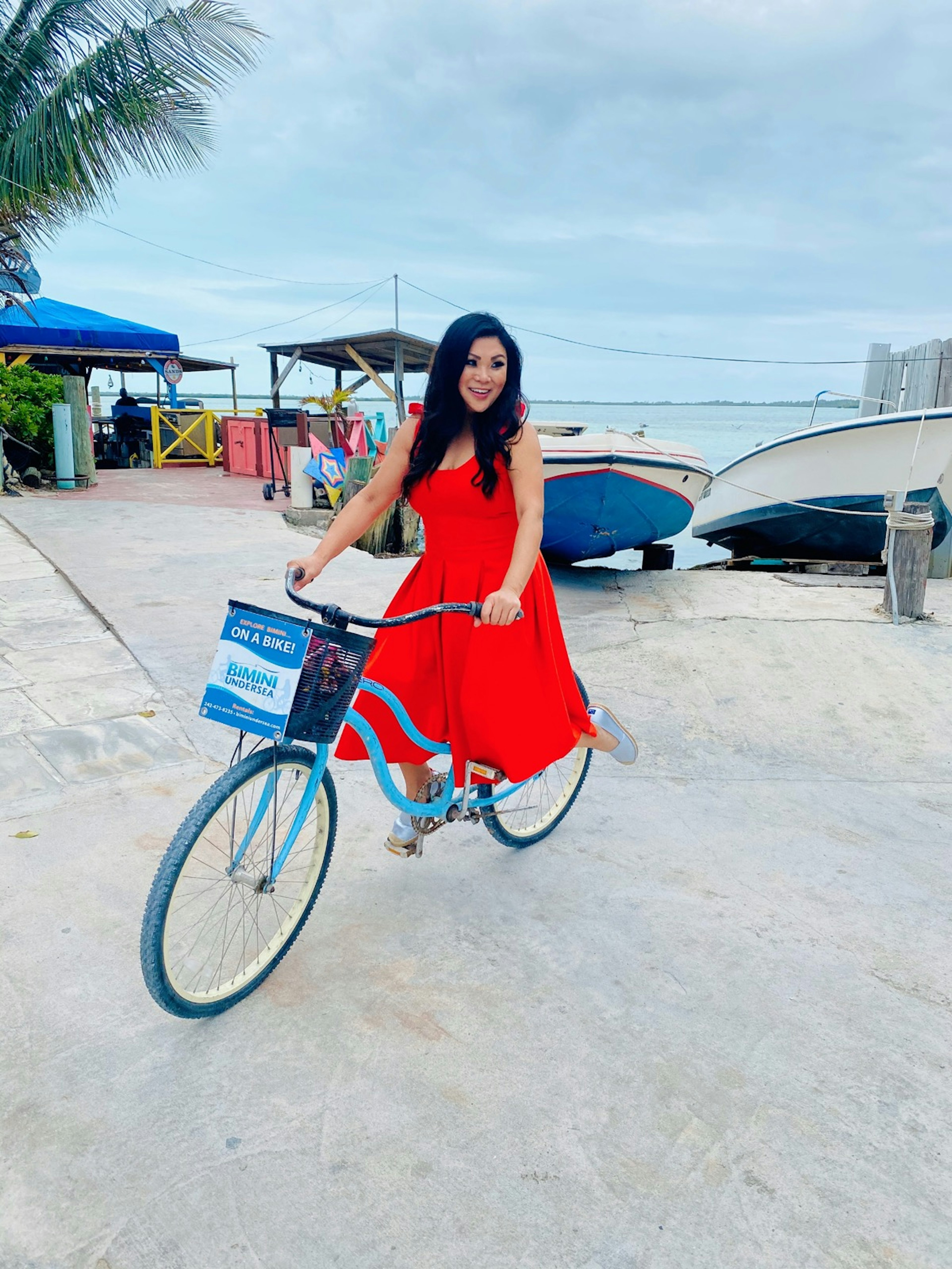 Woman on bike wearing a red dress near boats