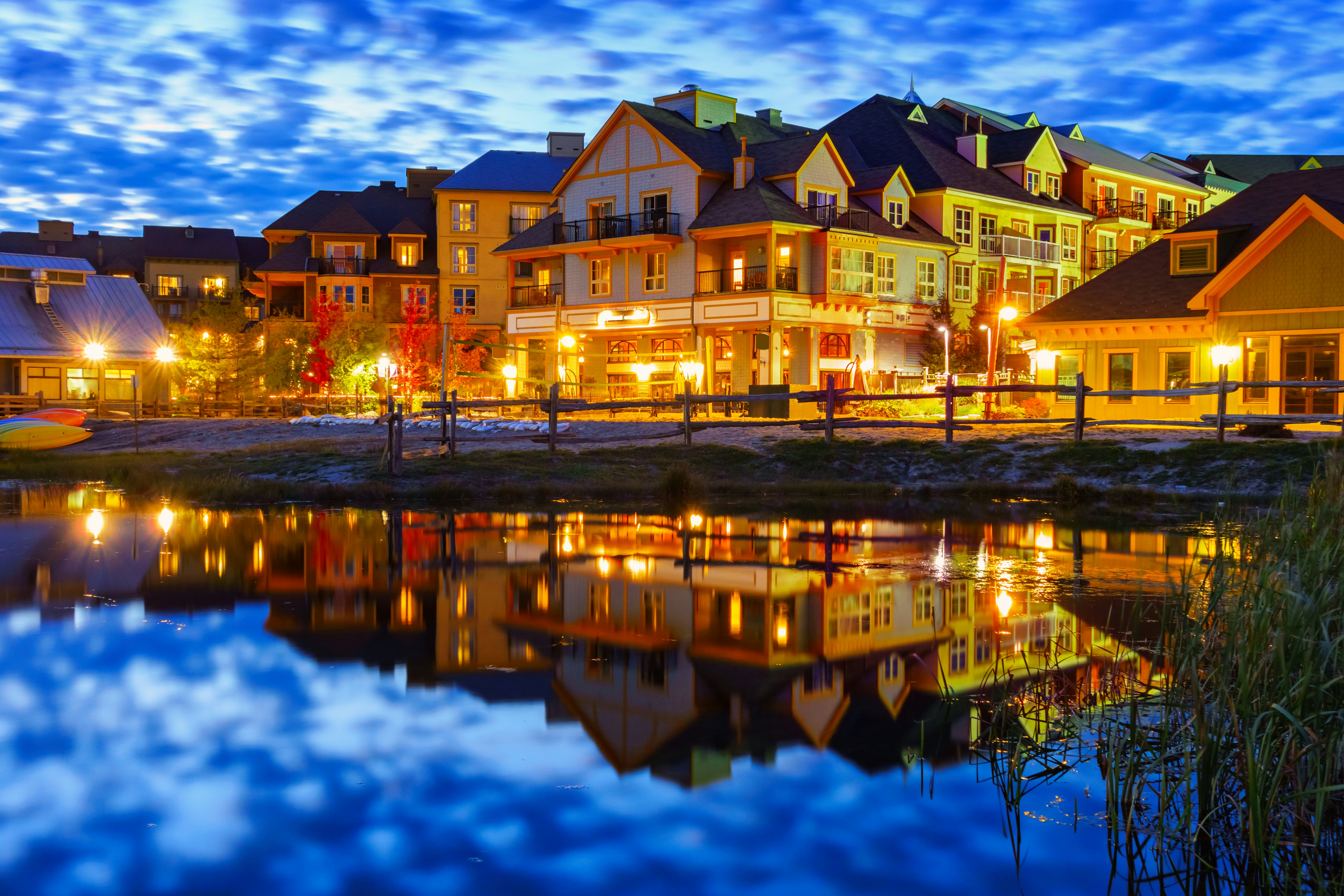 At twilight, brilliant yellow lights illuminate a charming small ski town reflected in a lake in the foreground; Toronto day trips