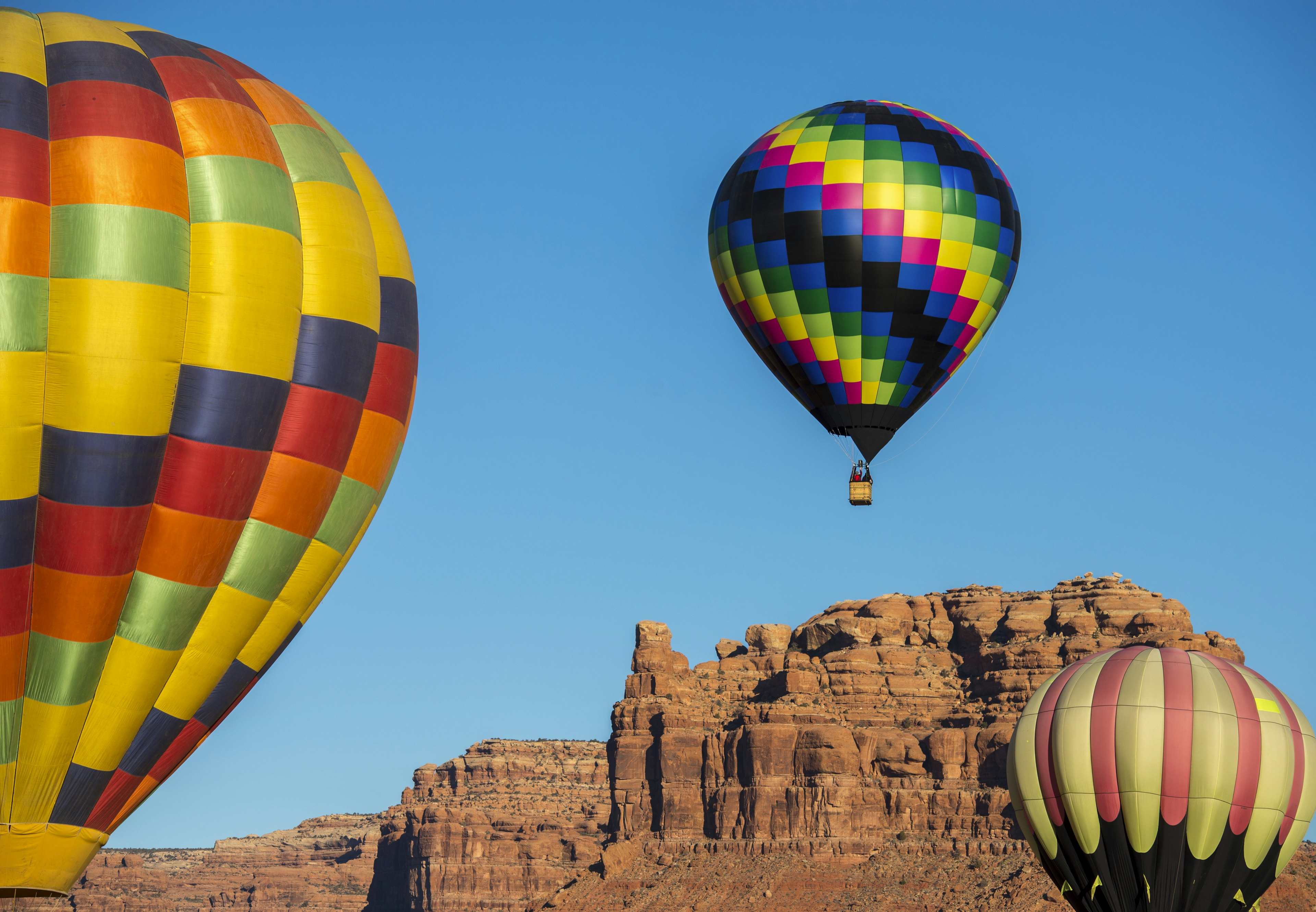 A trio of brightly colored hot air balloons soar around The Valley of the Gods during the Bluff International Balloon Festival.