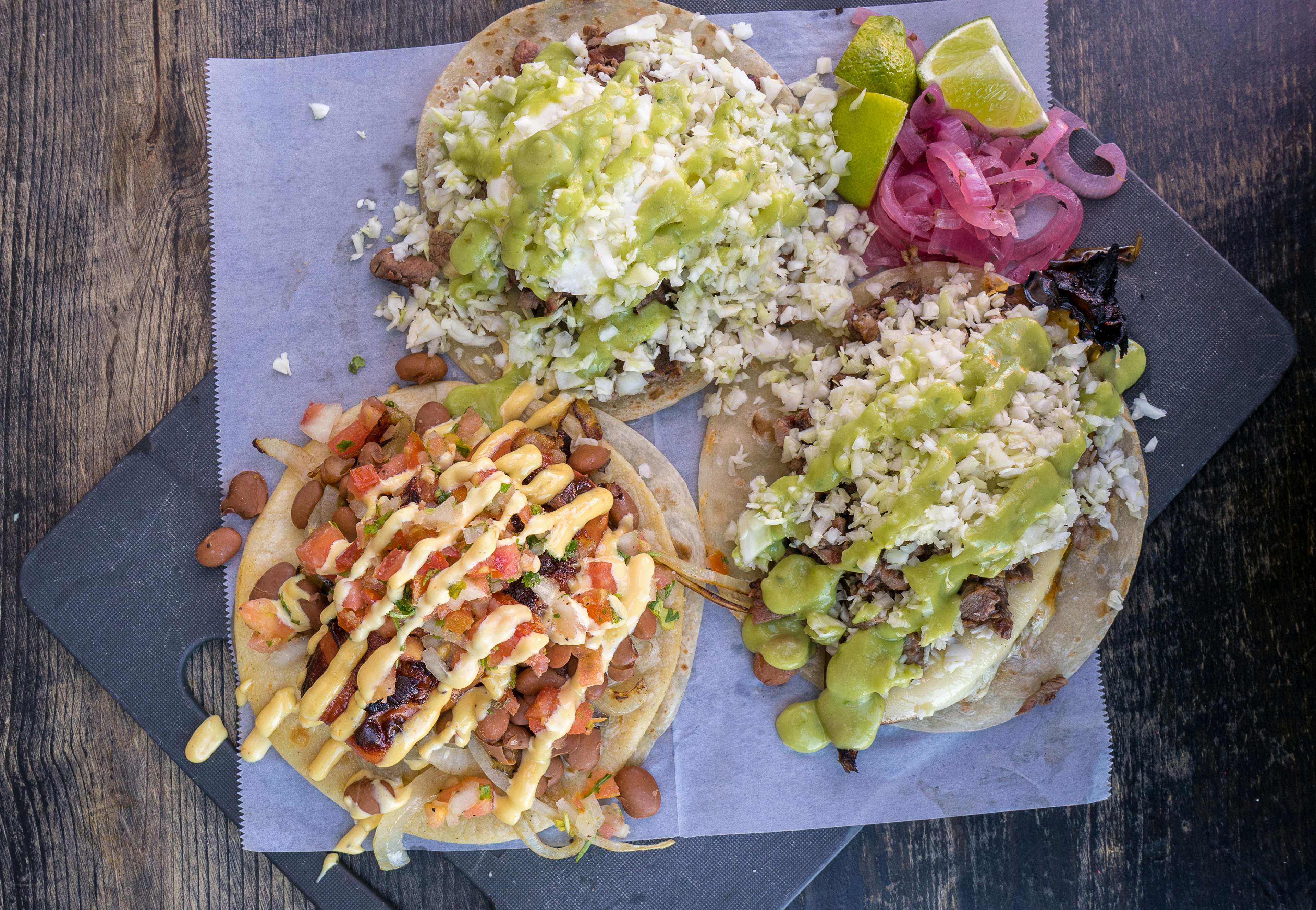 Three colorful tacos drizzled with assorted green and yellow sauces