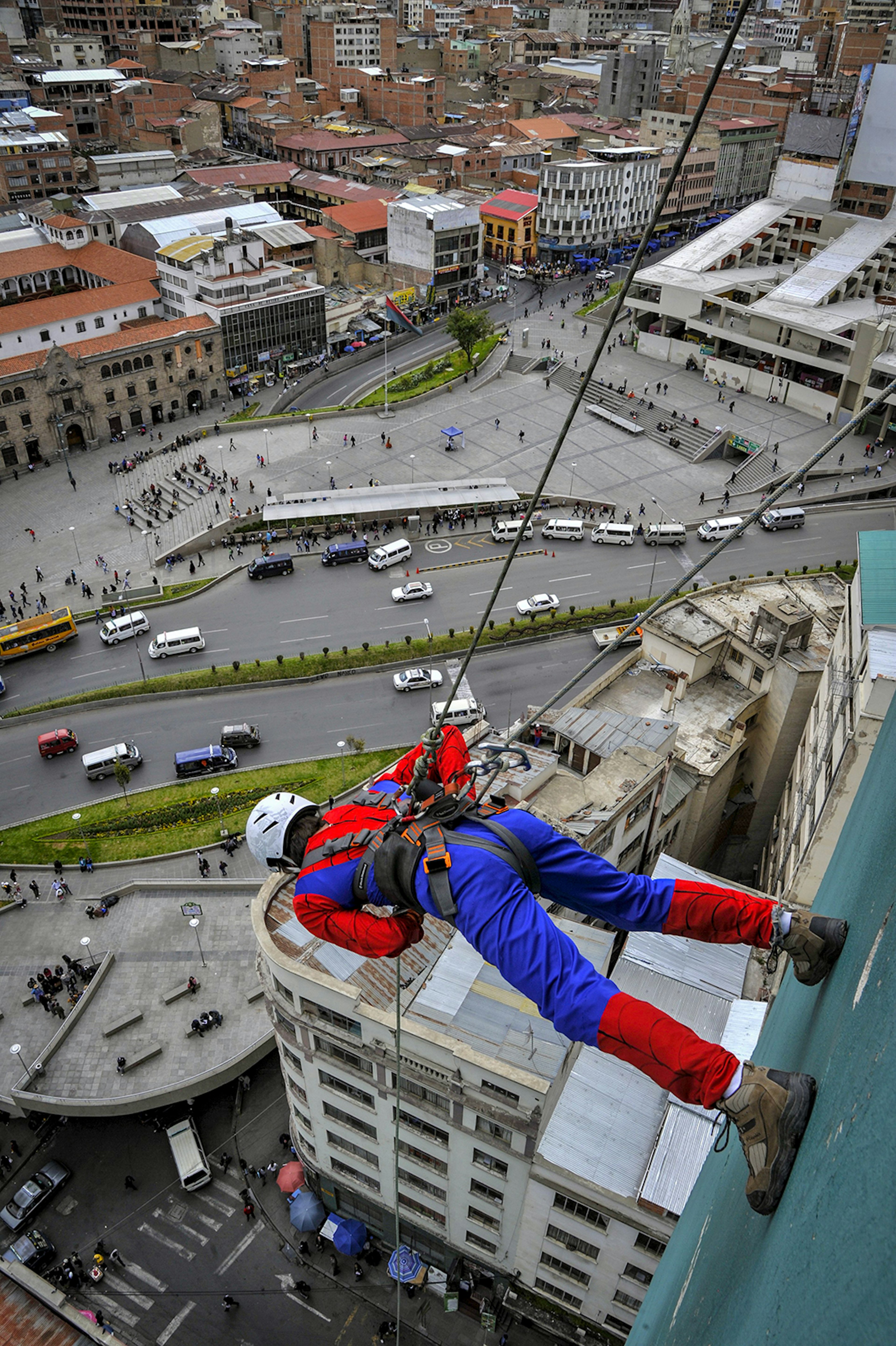 A man held by a tether stands on the wall of a tall building in La Paz and looks at the city below © AIZAR RALDES / Getty Images