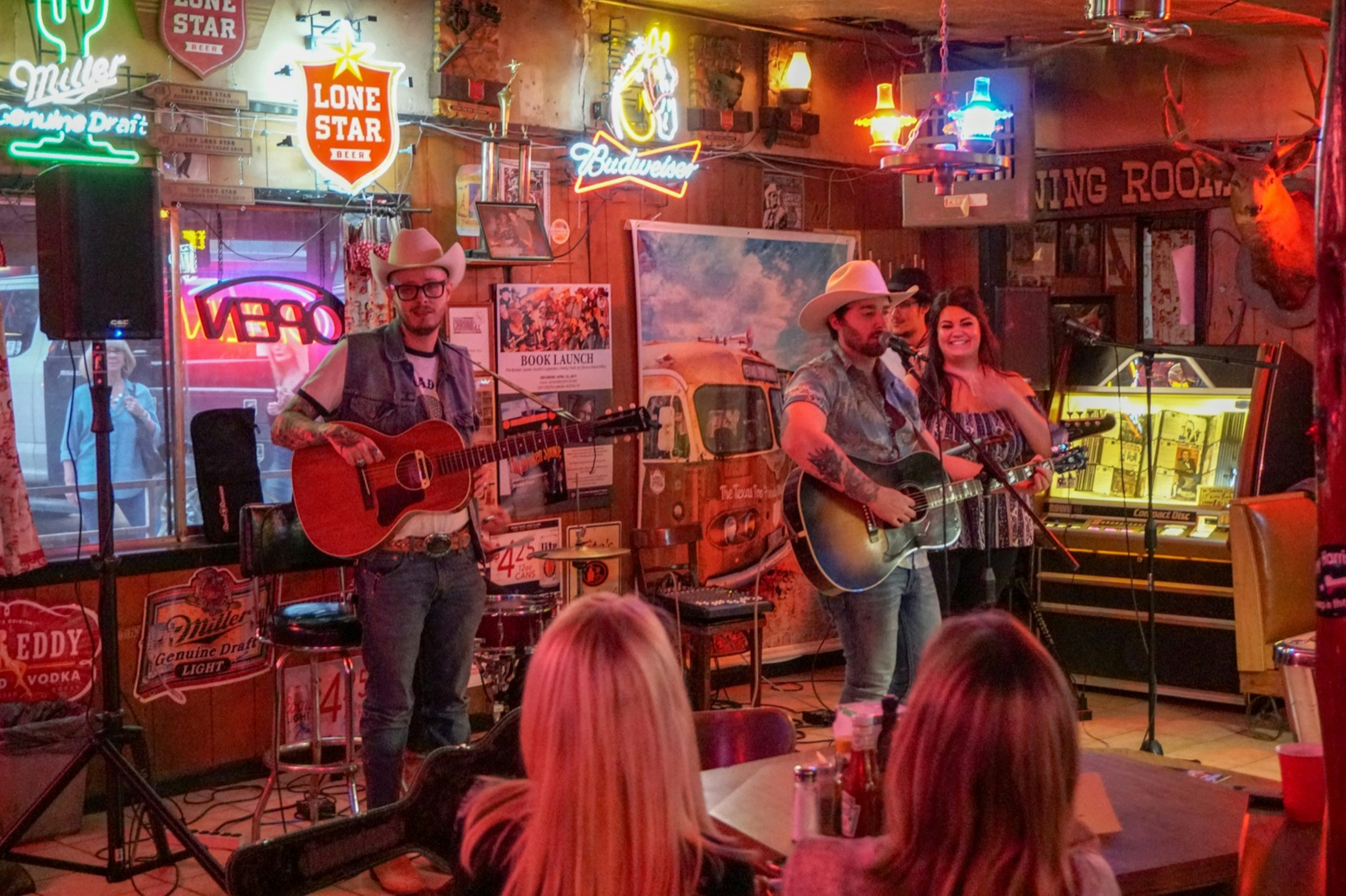 A country band is playing in the bar of a music hall as patrons watch from small tables in the cramped quarters in the Hill Country