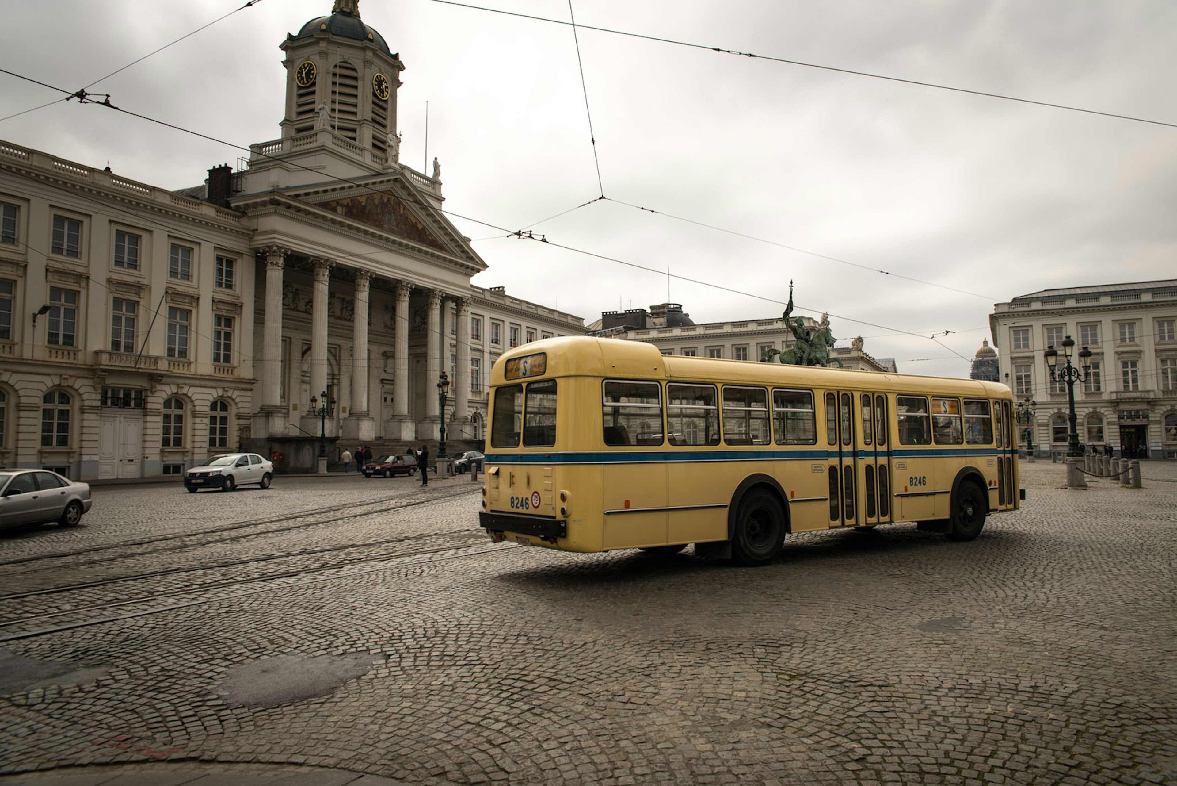 An old-fashioned yellow school bus parked in a large cobbled square in Brussels