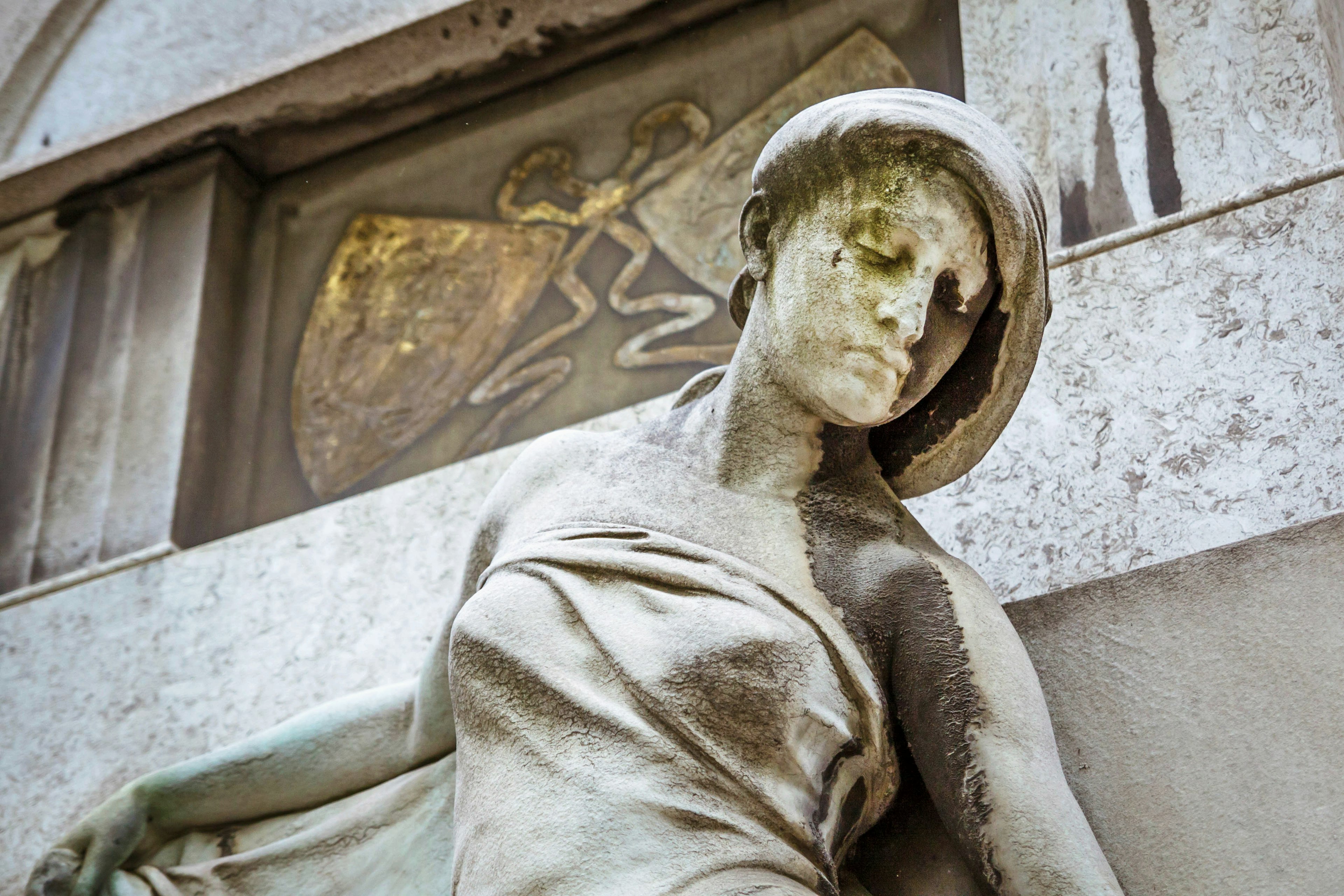 A closeup of statue of a women's face and upper body in front of a mausoleum at the Kerepesi Cemetery; Budapest autumn