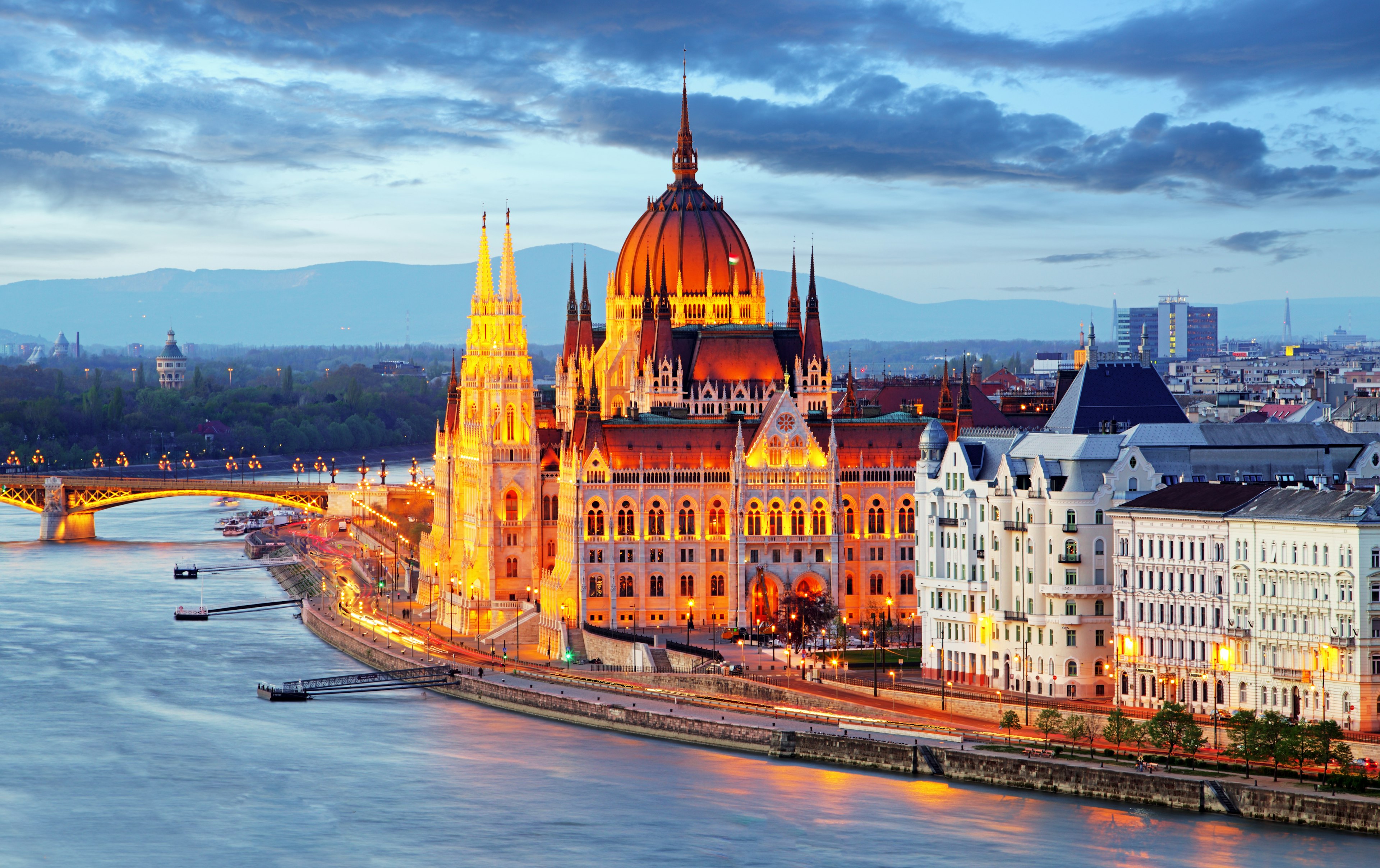 The Budapest Parliament located on the banks of the Danube, glows under a warm orange-yellow light during twilight. The surrounding buildings are illuminated by the street lights; Budapest autumn