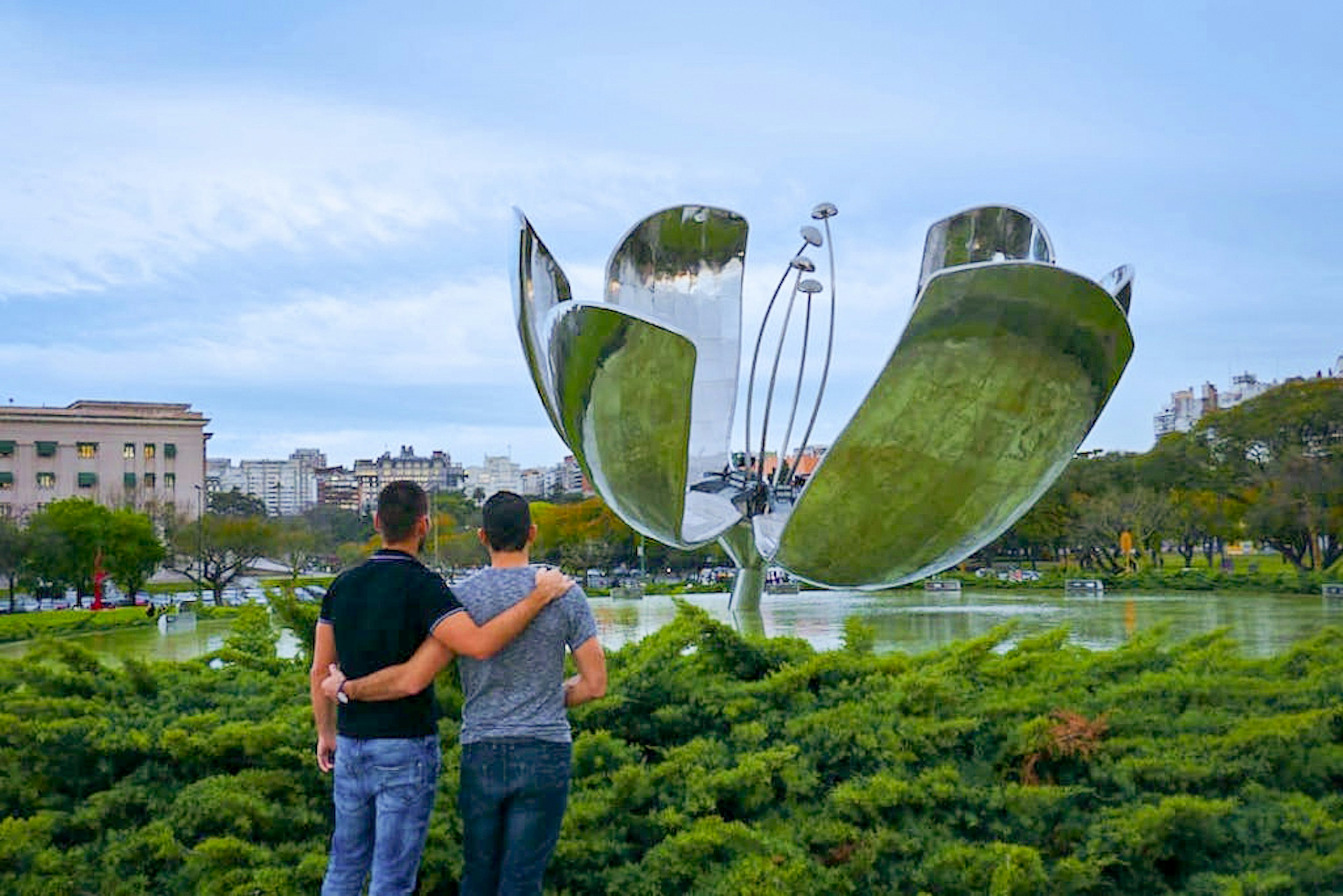 two men stand with arms around each other in front of large metal sculpture © Nomadic Boys / ϰϲʿ¼