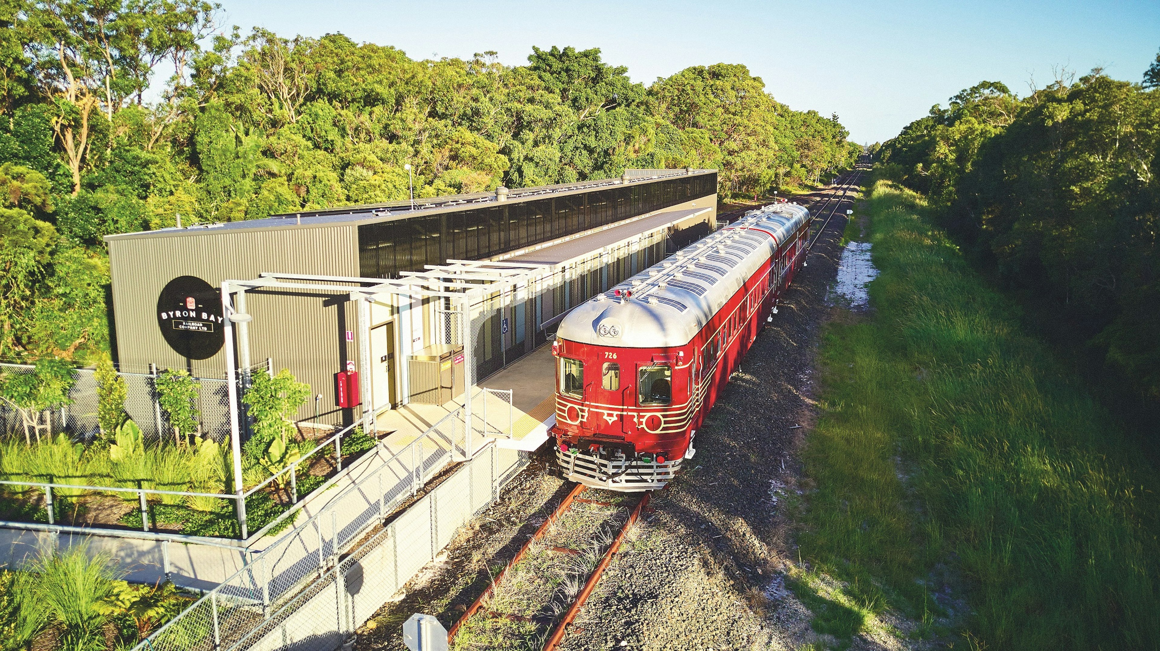 A red, two-carriage train stands outside a station. The roof of the train is covered in solar panels.